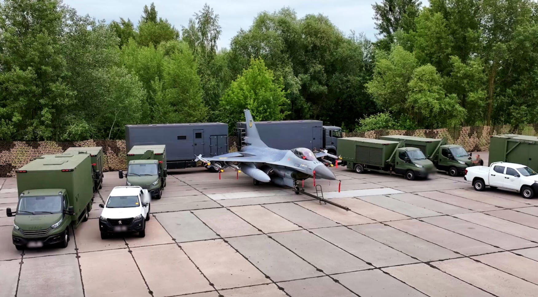 A grey fighter jet surrounded by green, white, and grey stuck in front of some trees