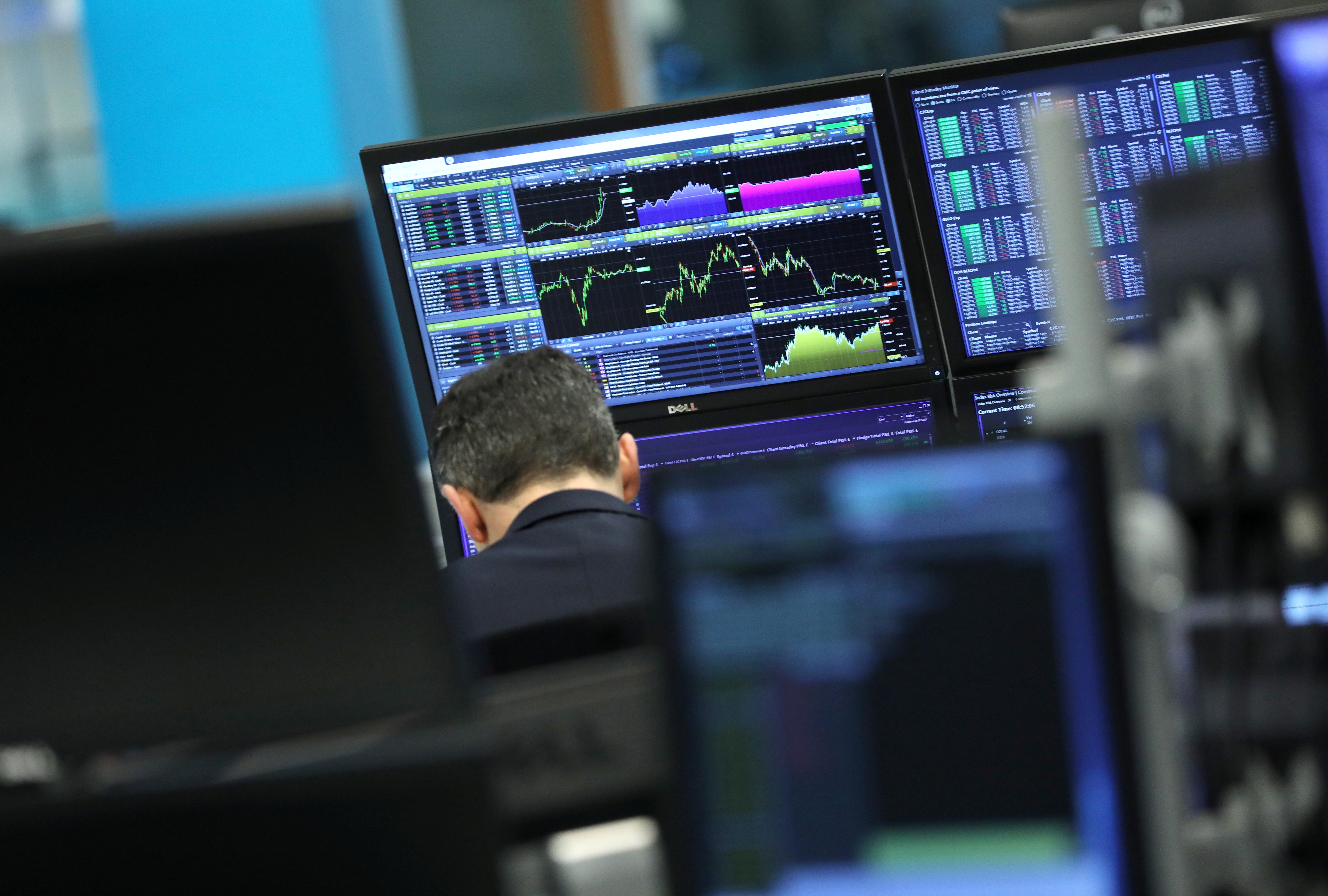 FILE PHOTO: A trader works as screens show market data at CMC markets in London, Britain, December 11, 2018. REUTERS/Simon Dawson