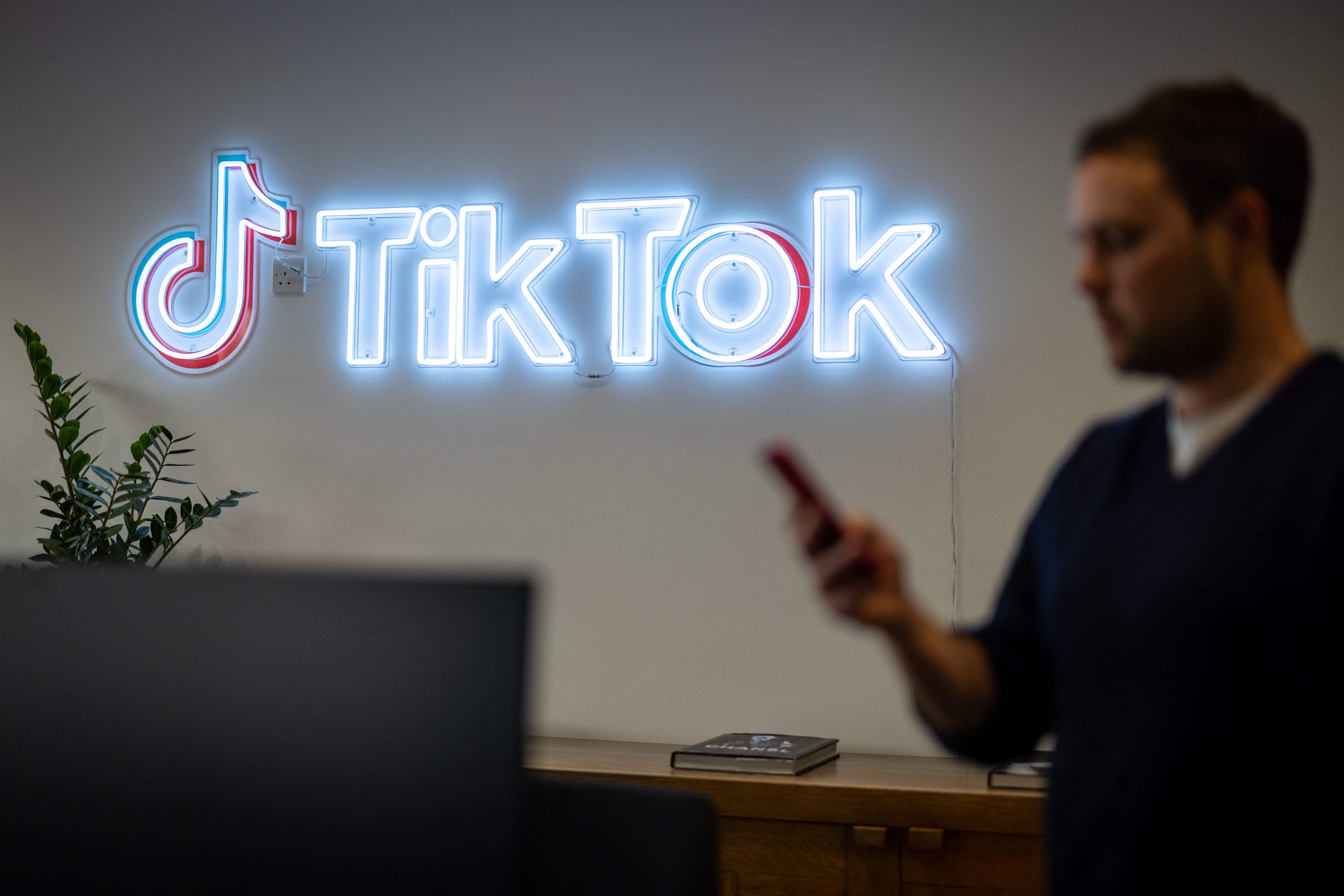 An employee looks at his mobile phone as he walks past the logo of TikTok at its office in London. 
