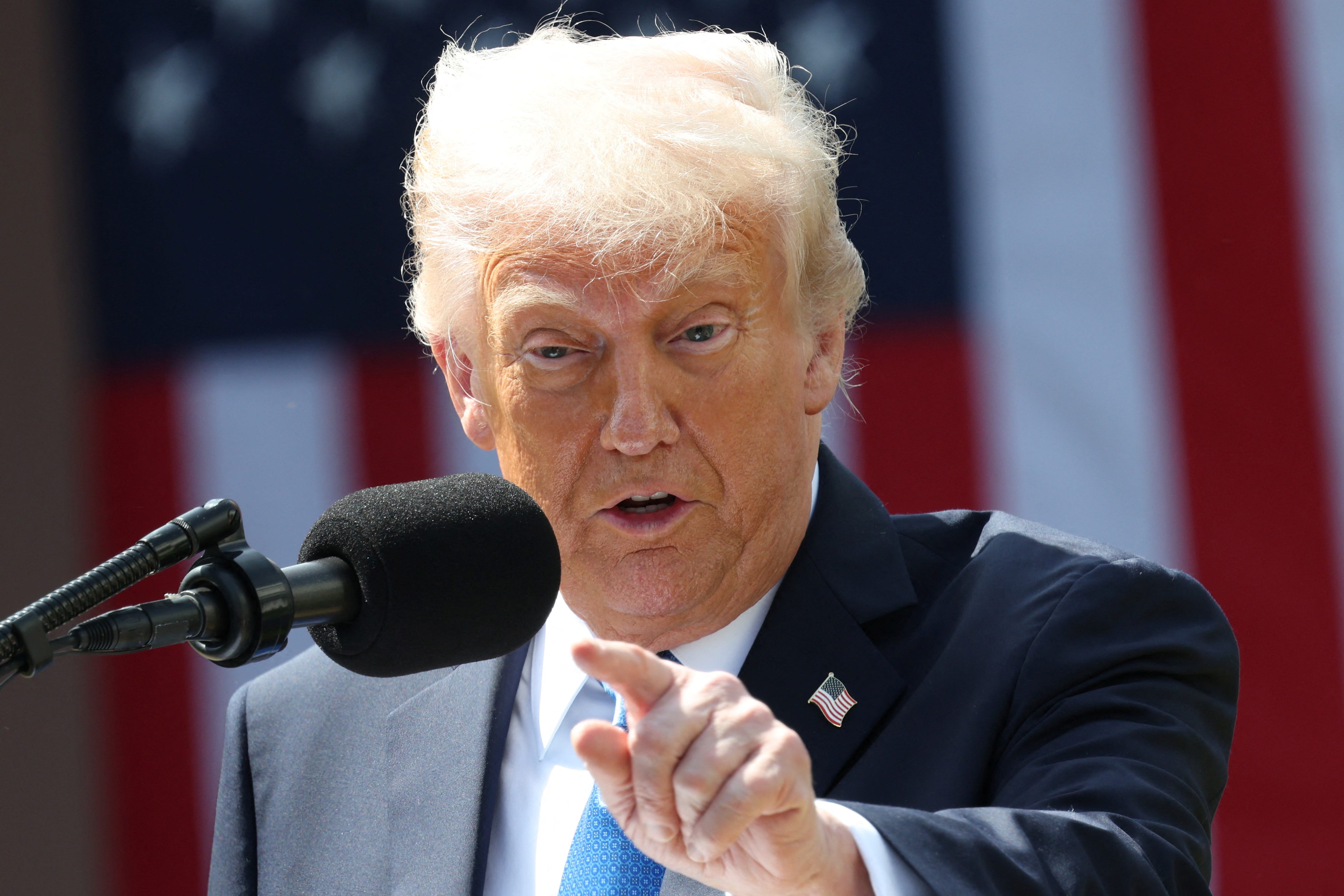 President Donald Trump speaking into a microphone and pointing. The US flag is behind him.