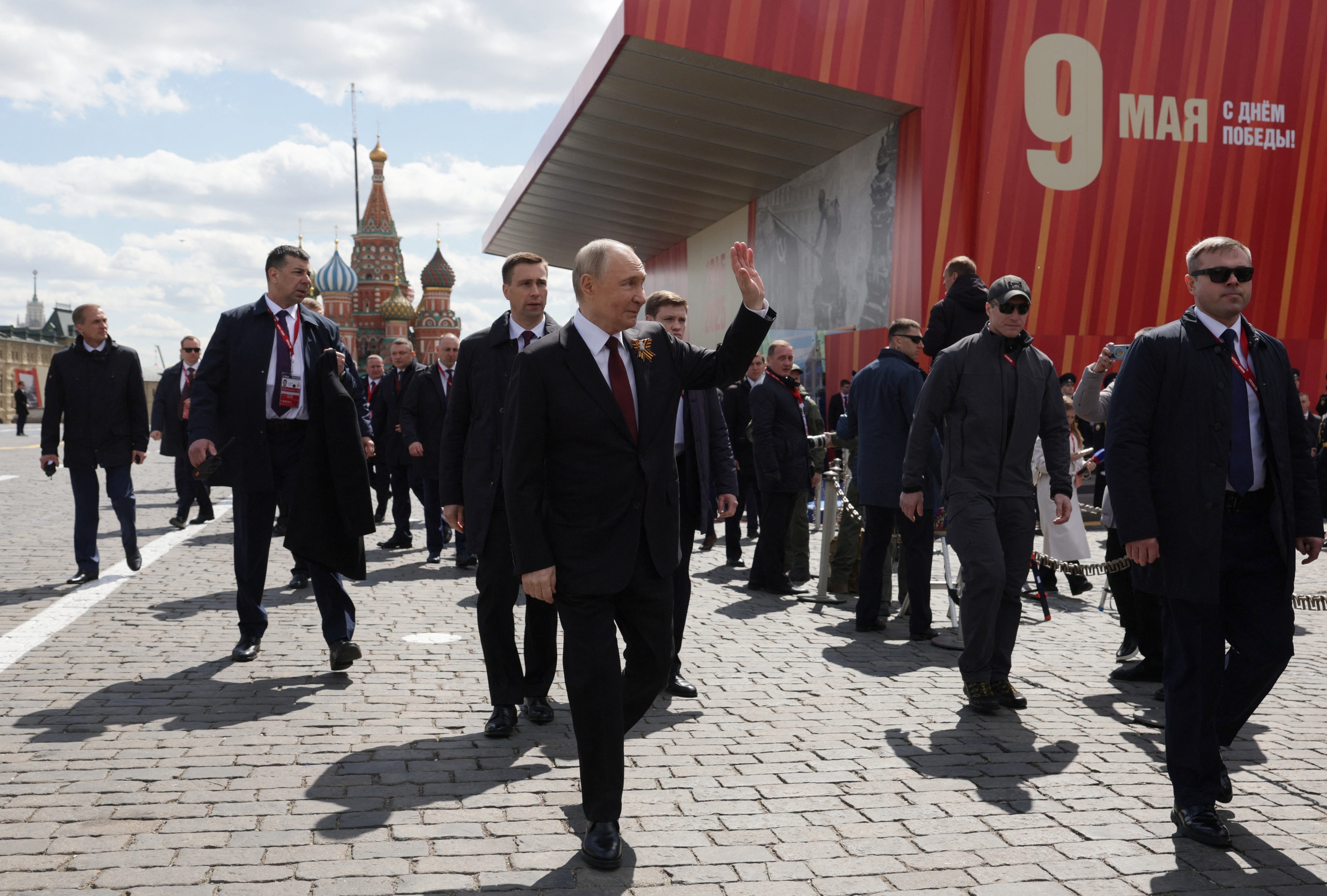 Putin waves to the crowd as he is flanked by bodyguards and staff.