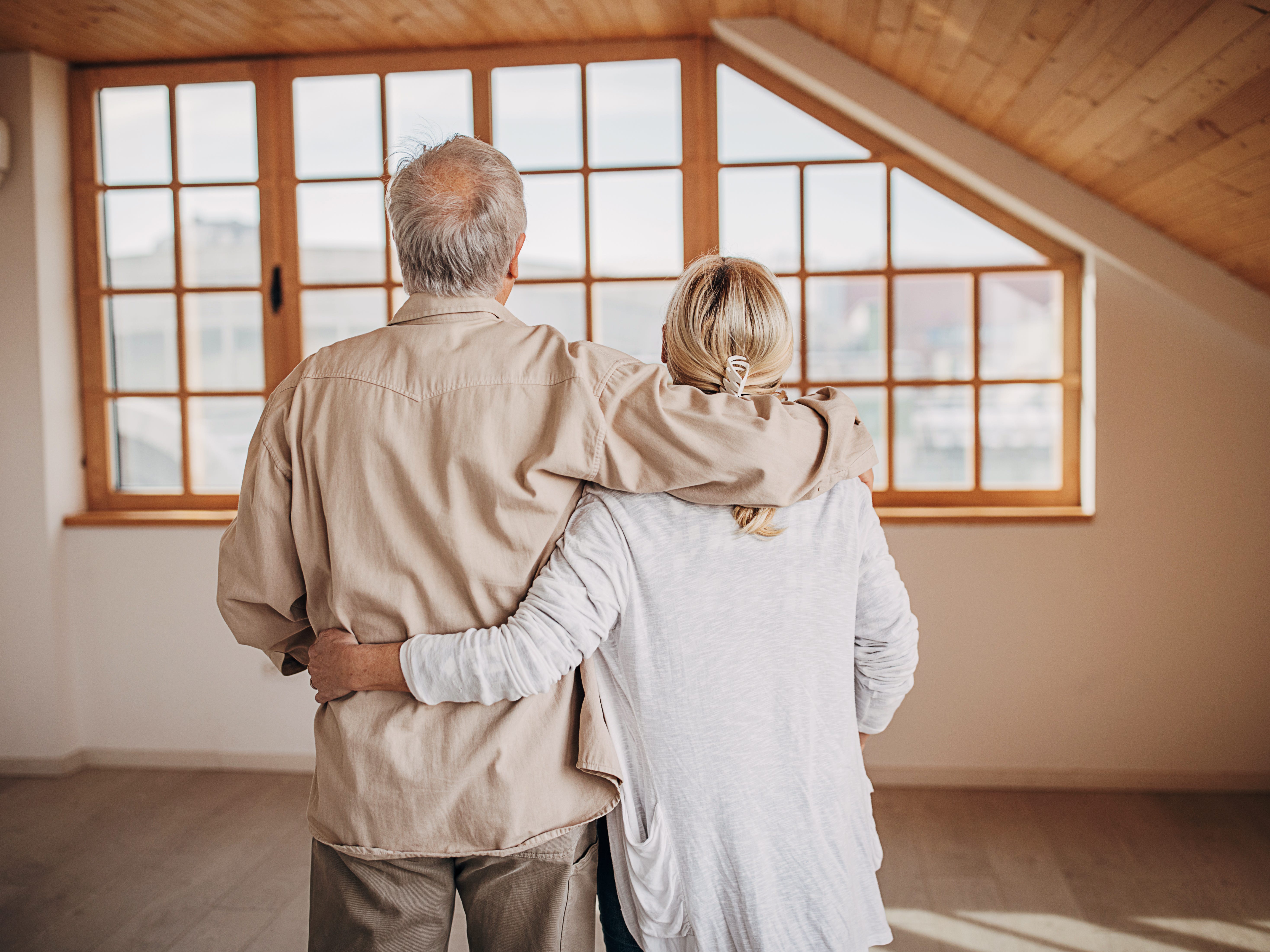 senior couple hugging and looking out window of house