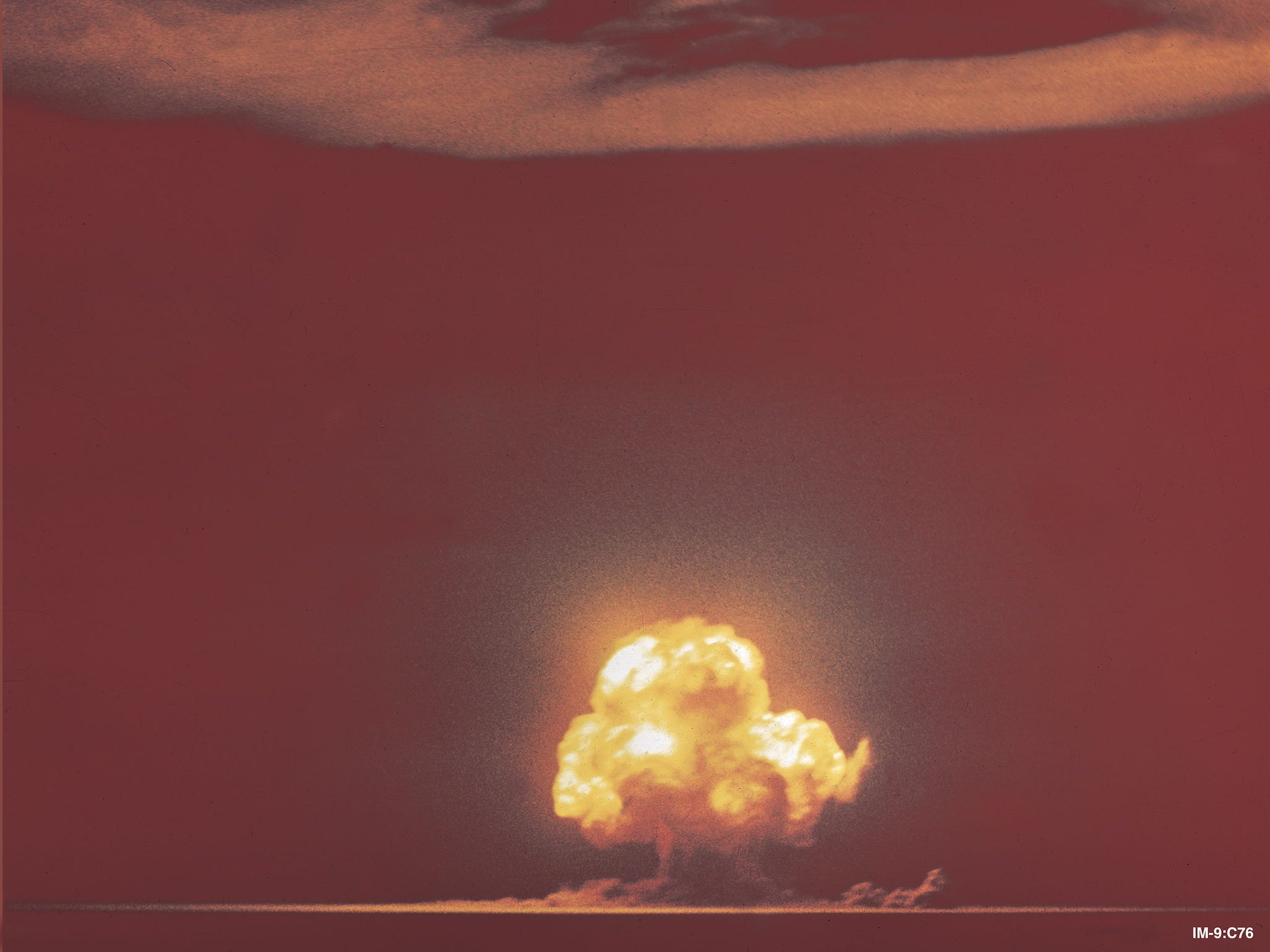 trinity nuclear bomb test distant yellow mushroom cloud erupting into orange sky