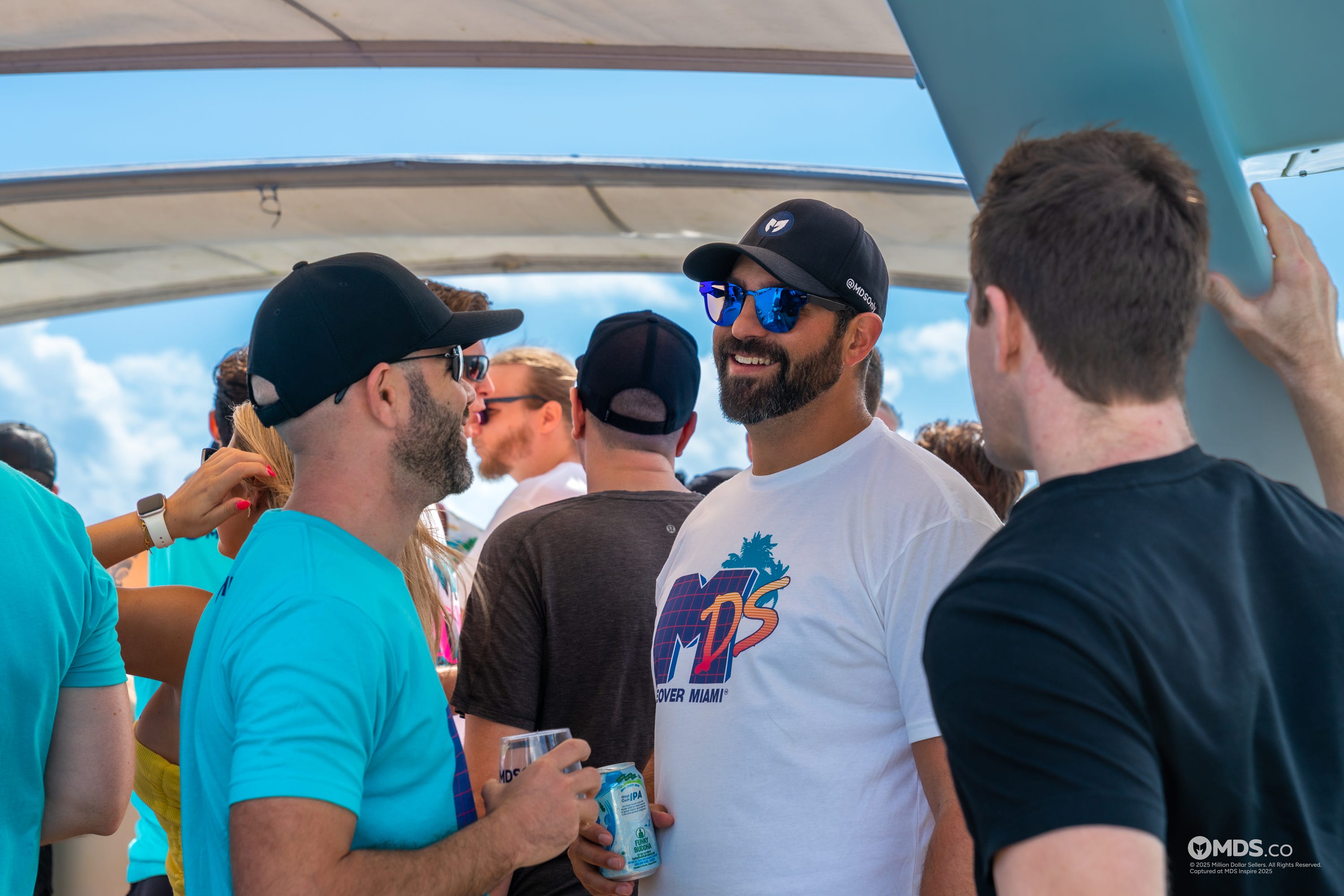 Three men with drinks in their hands talking to each other, while a crowd stands around them