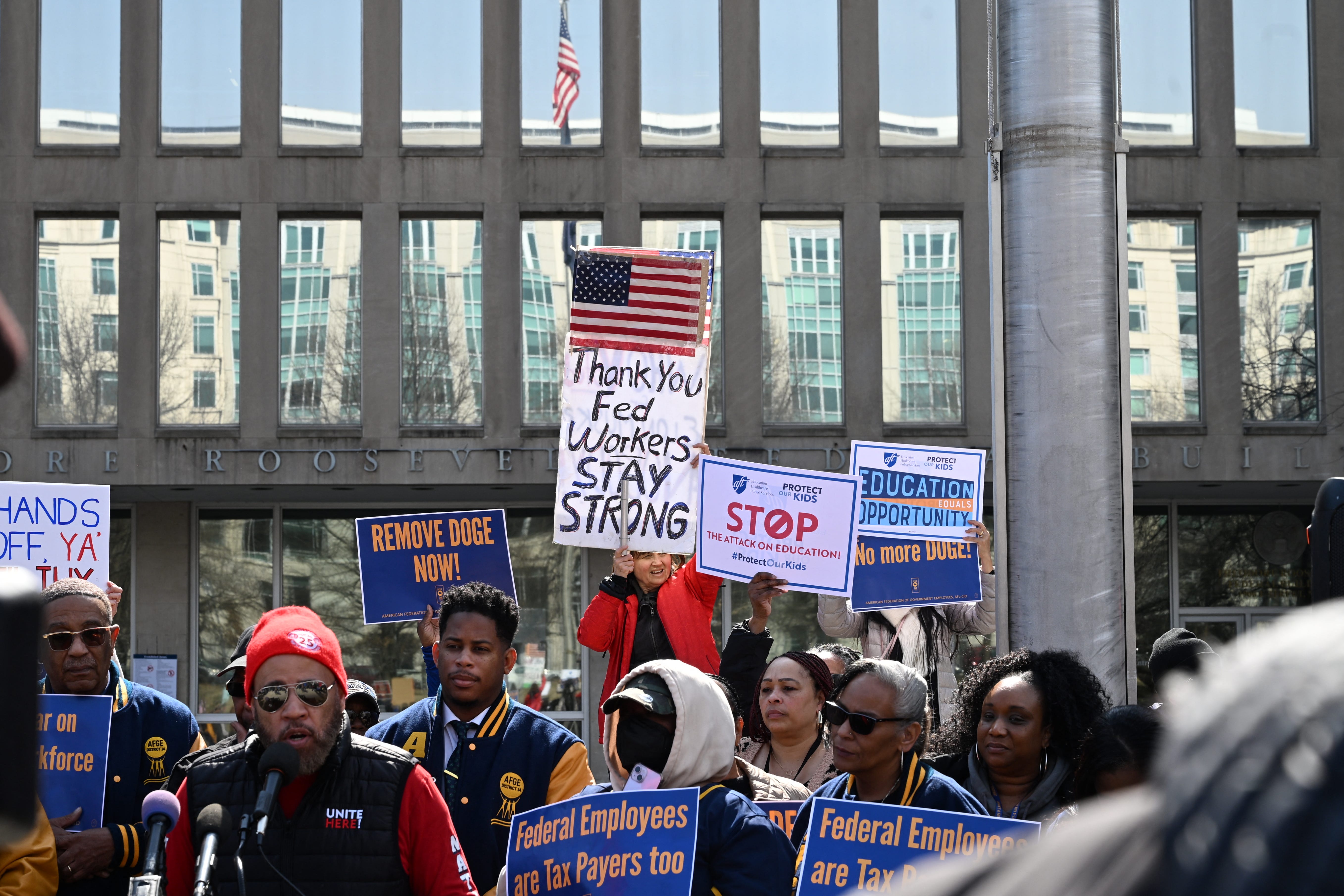 People with signs, including ones about DOGE or federal workers