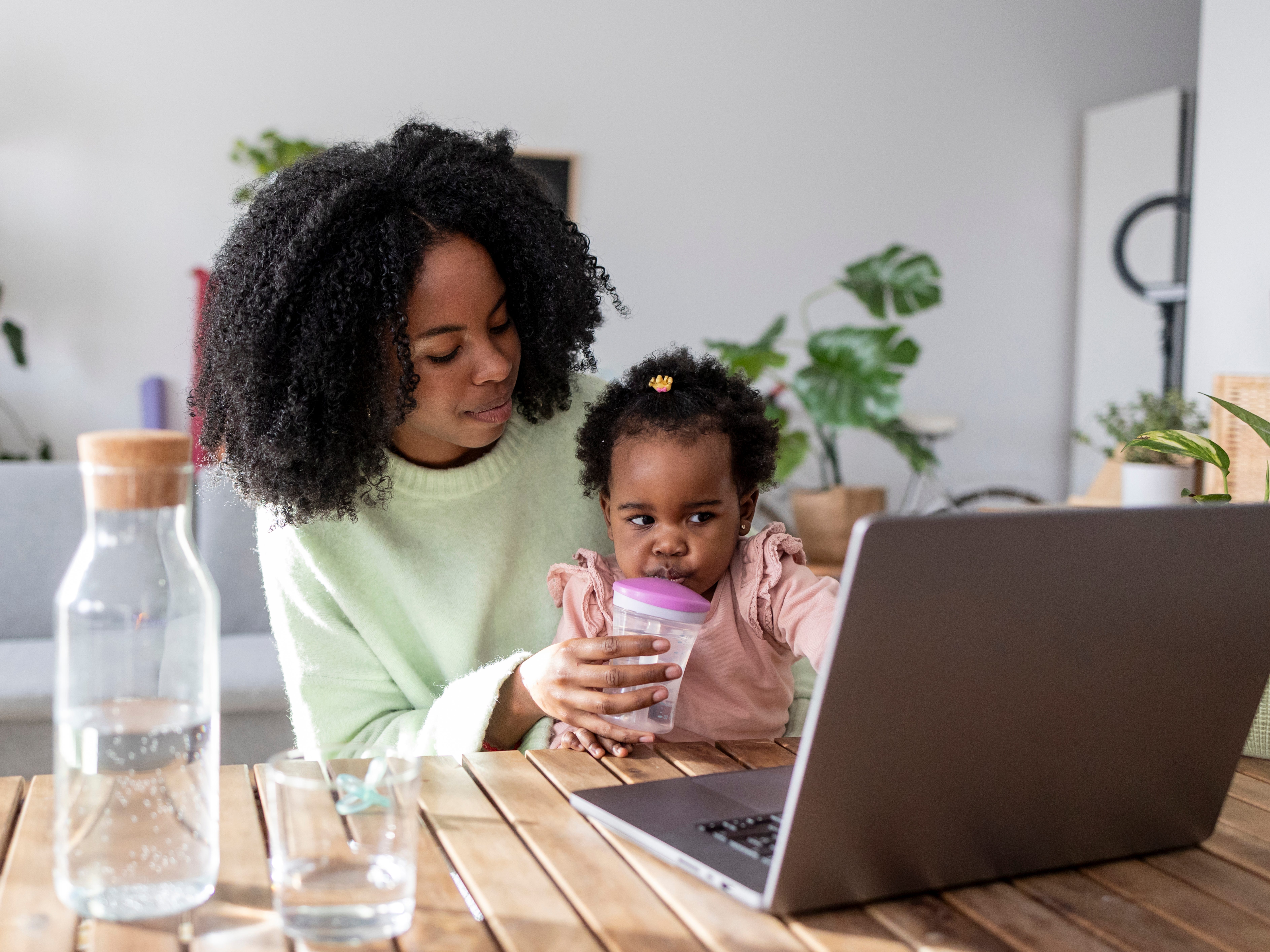 a wp,am holding her baby while looking at her laptop