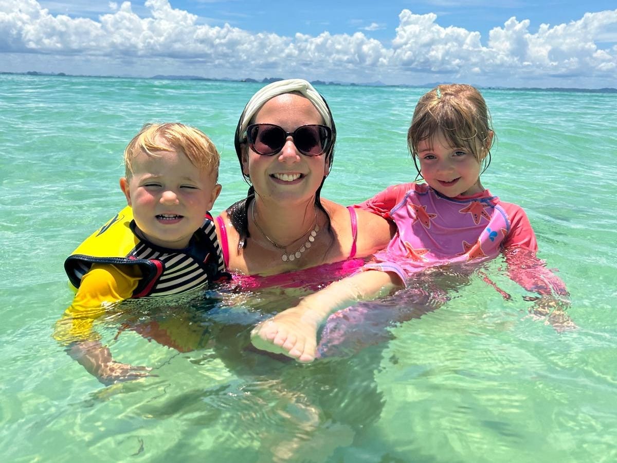 A woman poses while swimming in the ocean with two kids.