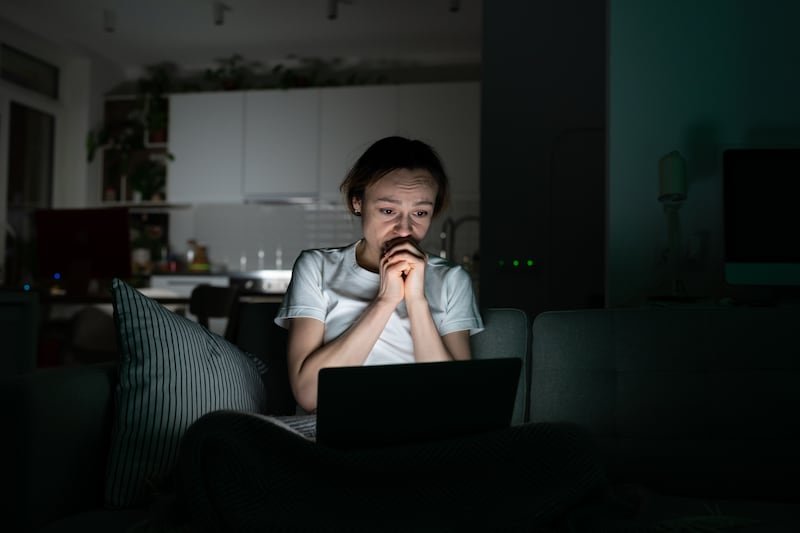Anxious young woman looking at laptop screen at night, read sudden bad news, very worried. Shocked female can not stop scrolling news media in computer before bedtime. Anxiety, mental health.