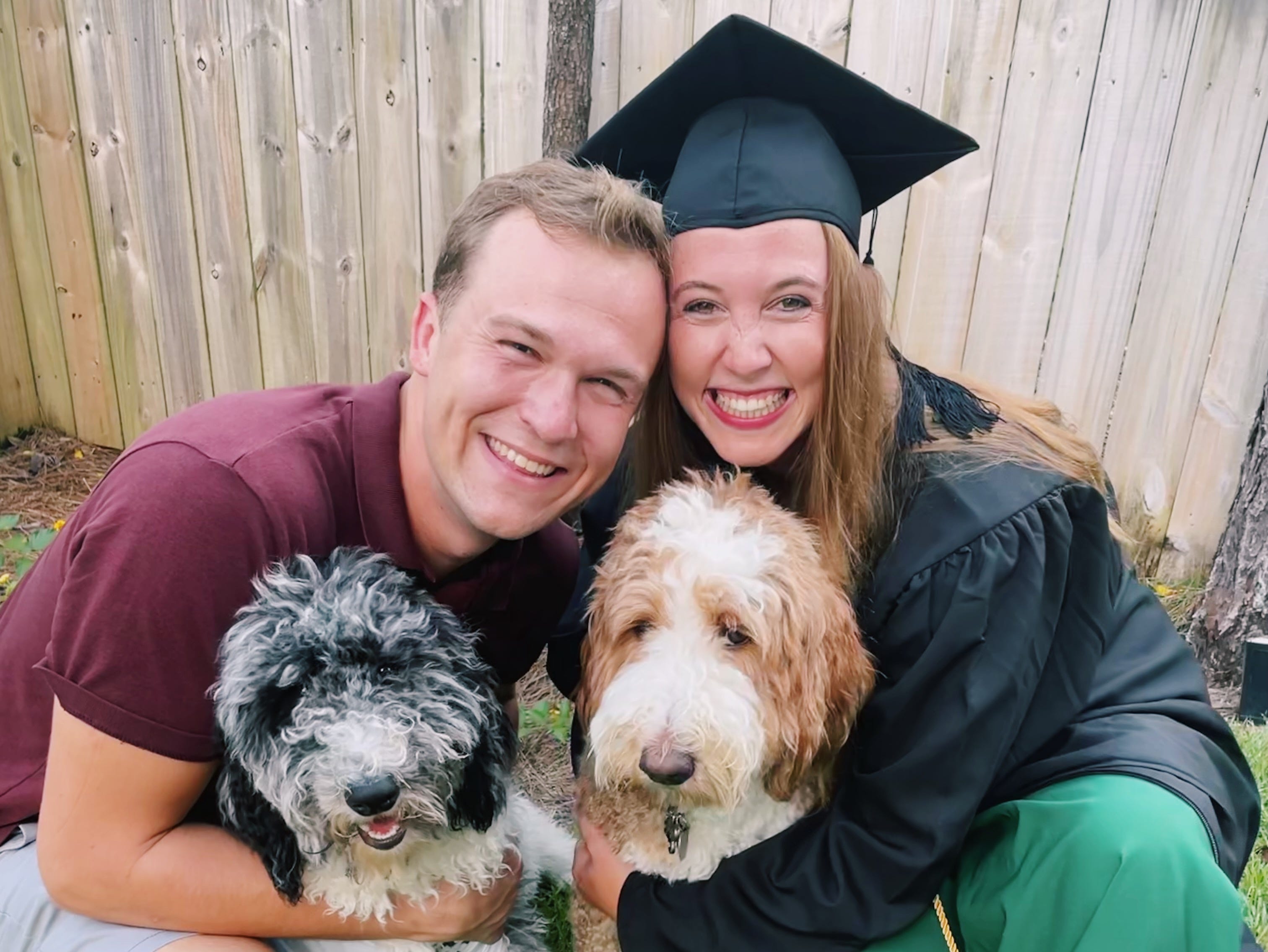 Allie Hubers in graduation cap with husband and two dogs