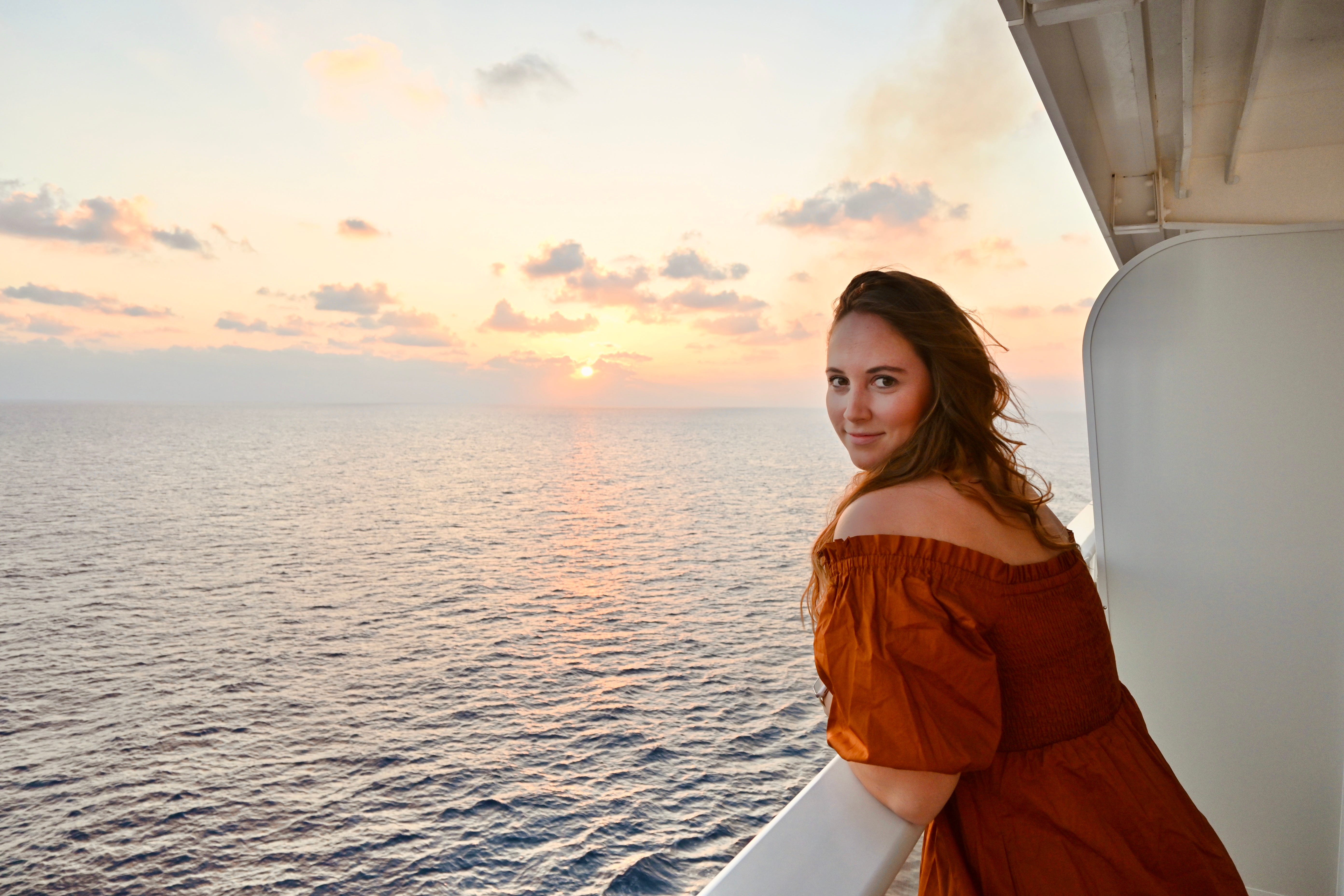 Author Allie Hubers leaning over balcony on boat at sunset