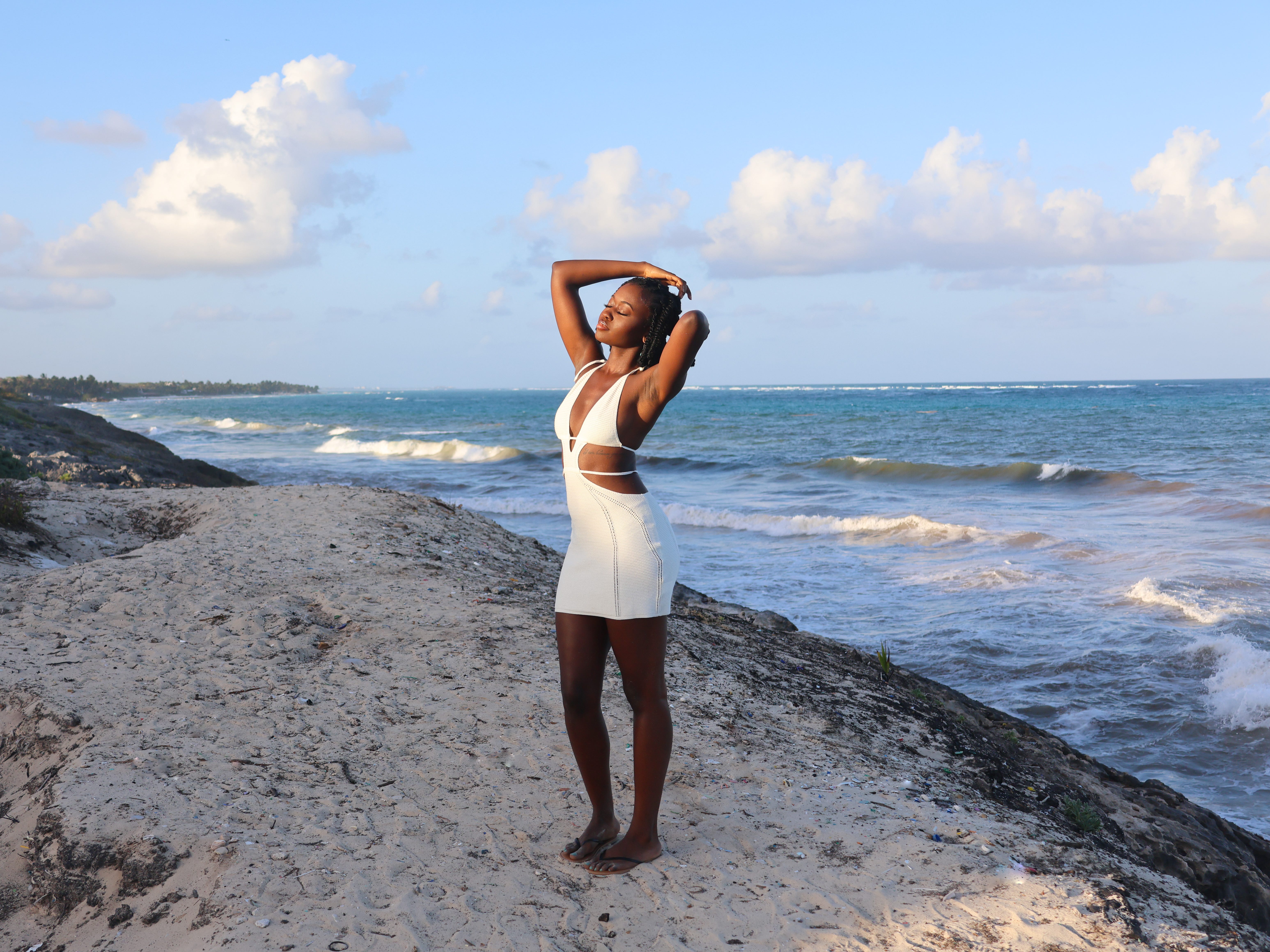 The author posing on a beach in Tulum in a white dress.