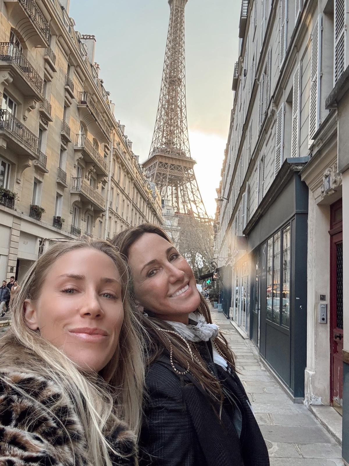 Two women smile in a selfie with the Eiffel Tower in the background.