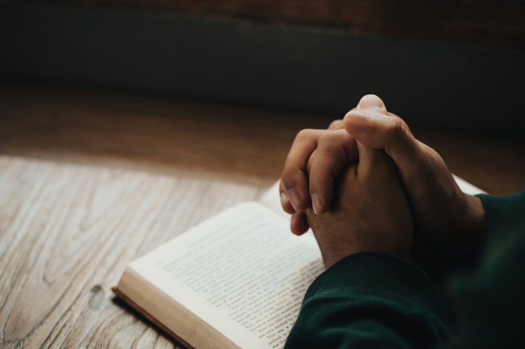 Person praying with hands clasped over an open Bible.