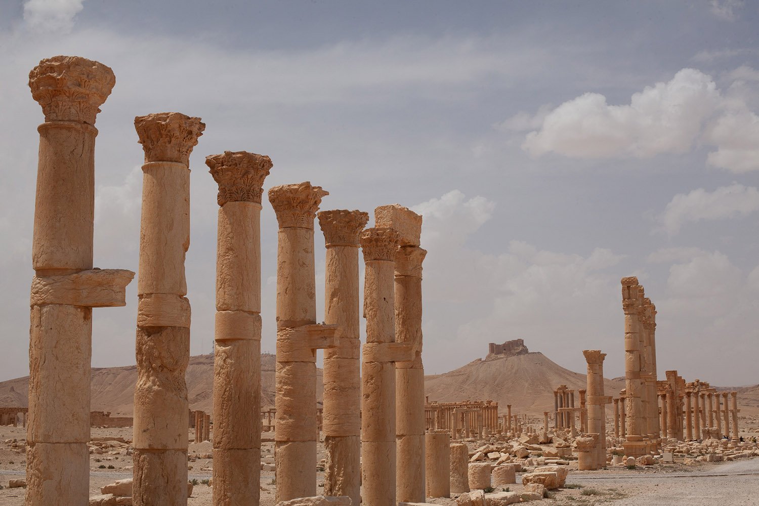 Giant Roman columns some heavily damaged. A fortress on the hill in the distance.