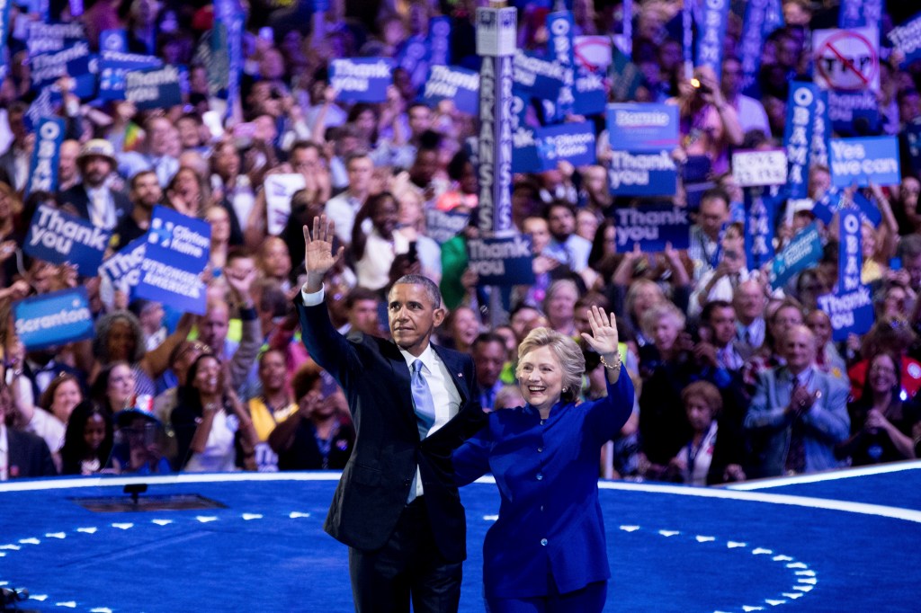 Obama and Clinton waving to a cheering crowd.