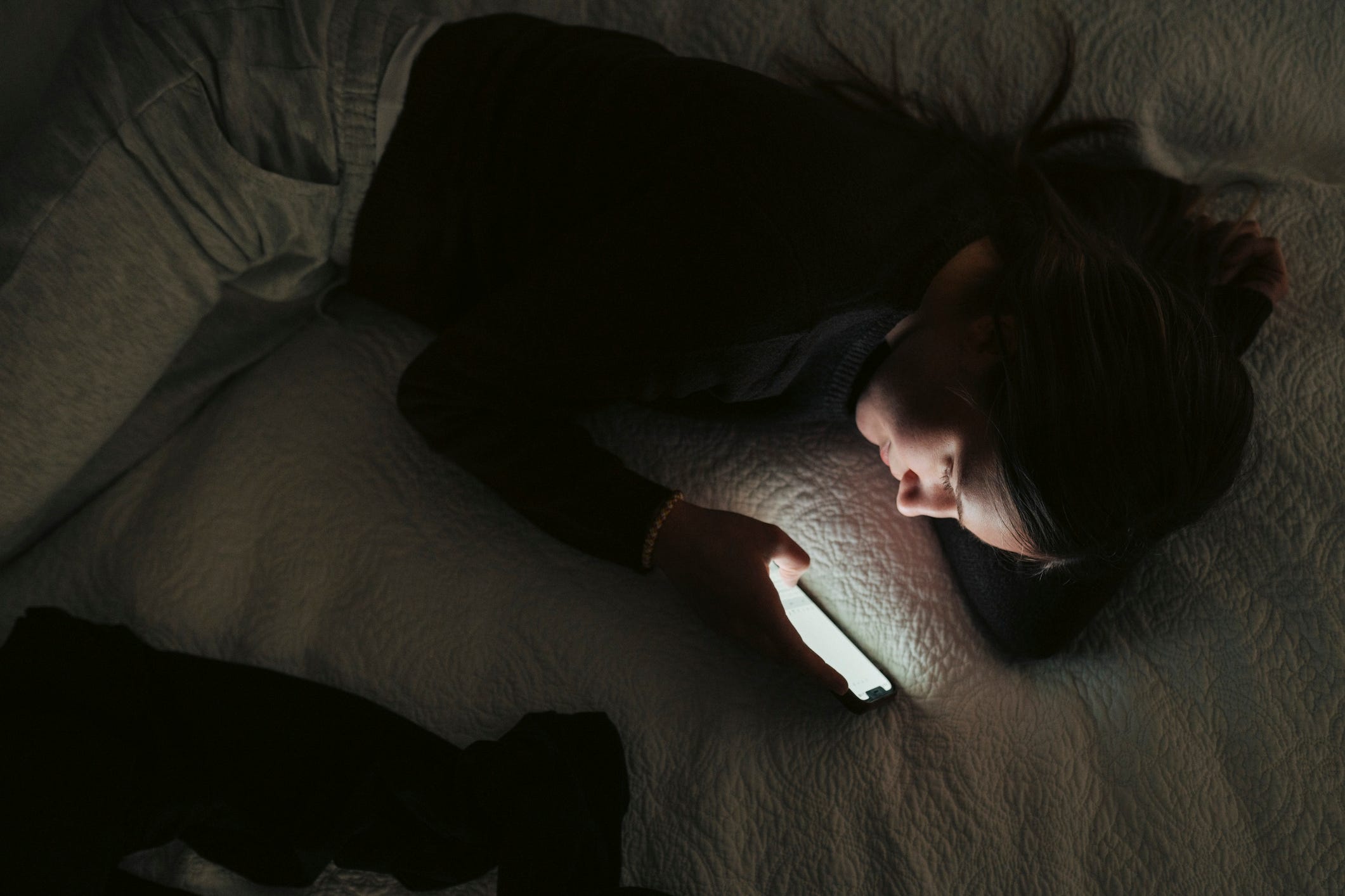 A teen girl in bed on a phone