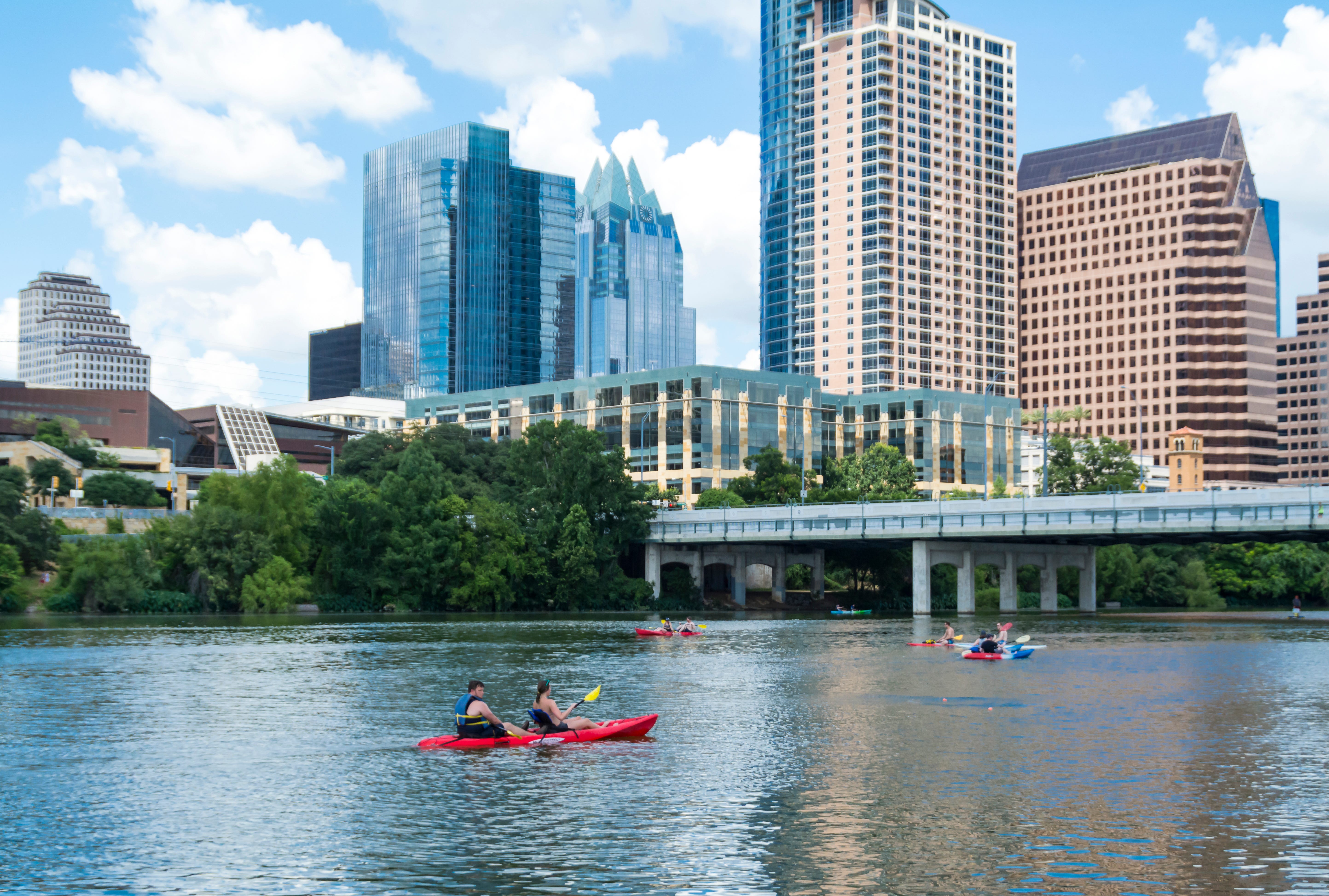 Two separate groups of people  kayaking on Lady Bird Lake in Austin with the city skyline above them.