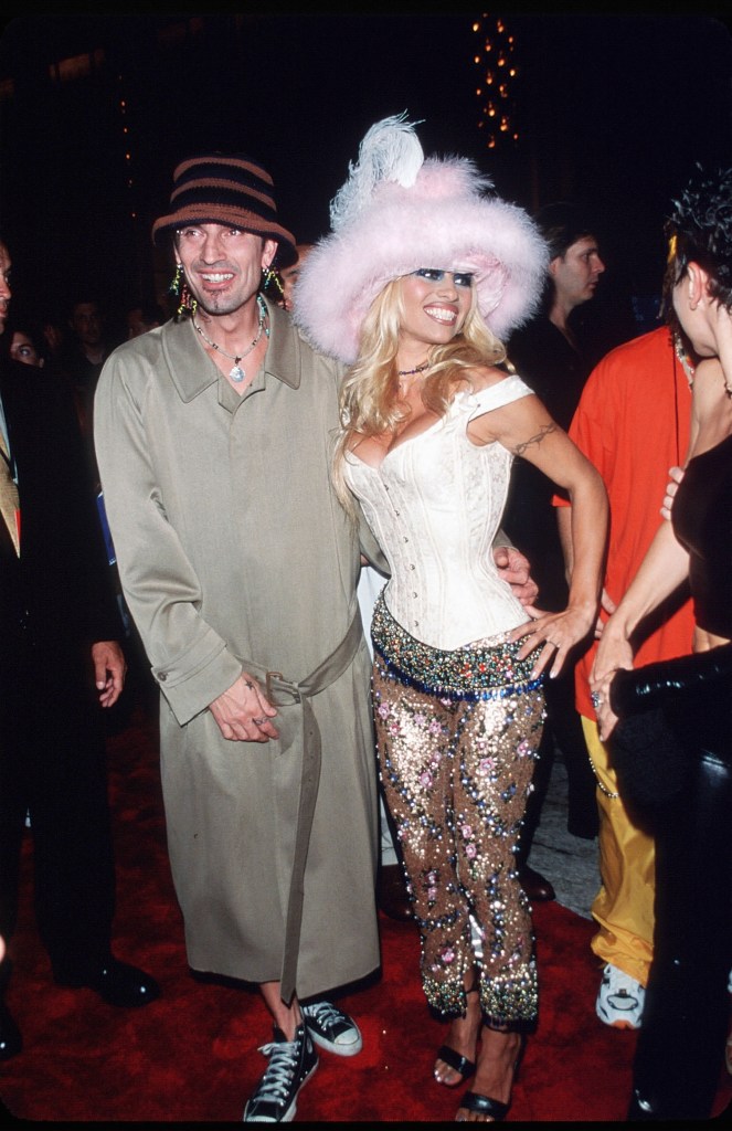 Pamela Anderson in a pink flurry hat, white bodice and sparkling, sheer skirt., Tommy Lee in a grey coat and sneakers.