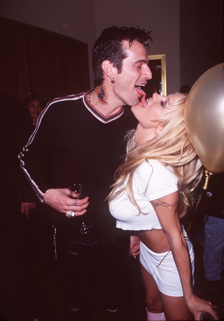 Pamela Anderson in a cropped white t-shirt and mini-skirt, kisses Tommy Lee, in a black top with stripes down the sleeves and black pants.