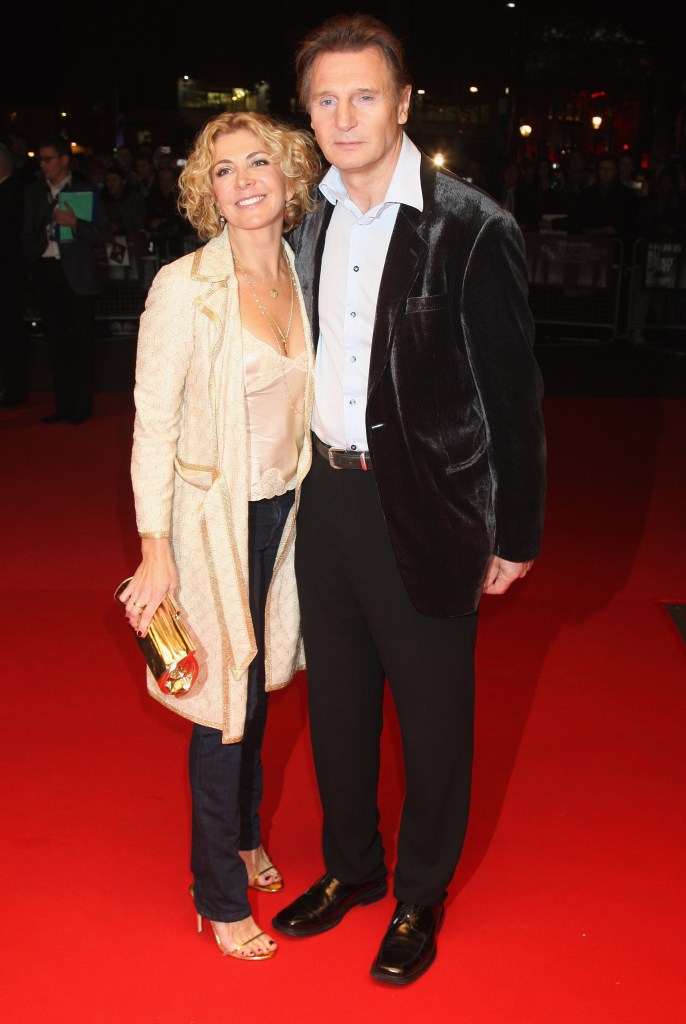 Liam Neeson in a dark brown velvet blazer and black pants and a white shirt, Natasha Richardson in a cream coat, cream top and black pants.