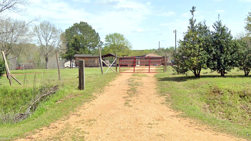 Charles Sims' cult compound in Silver Creek , Mo seen here with dirt road leading up to a red fence with some trees in background.