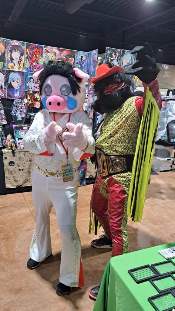 Photo of two people in costume at Squonkapalooza 2024.  One is dressed as Elvis Presley, the other as Mothman Randy Savage.