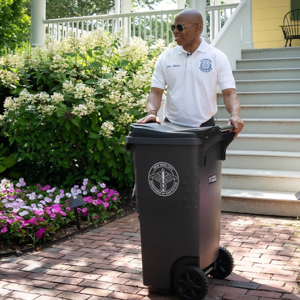 Eric Adams pushing a New York City Department of Sanitation trash can.