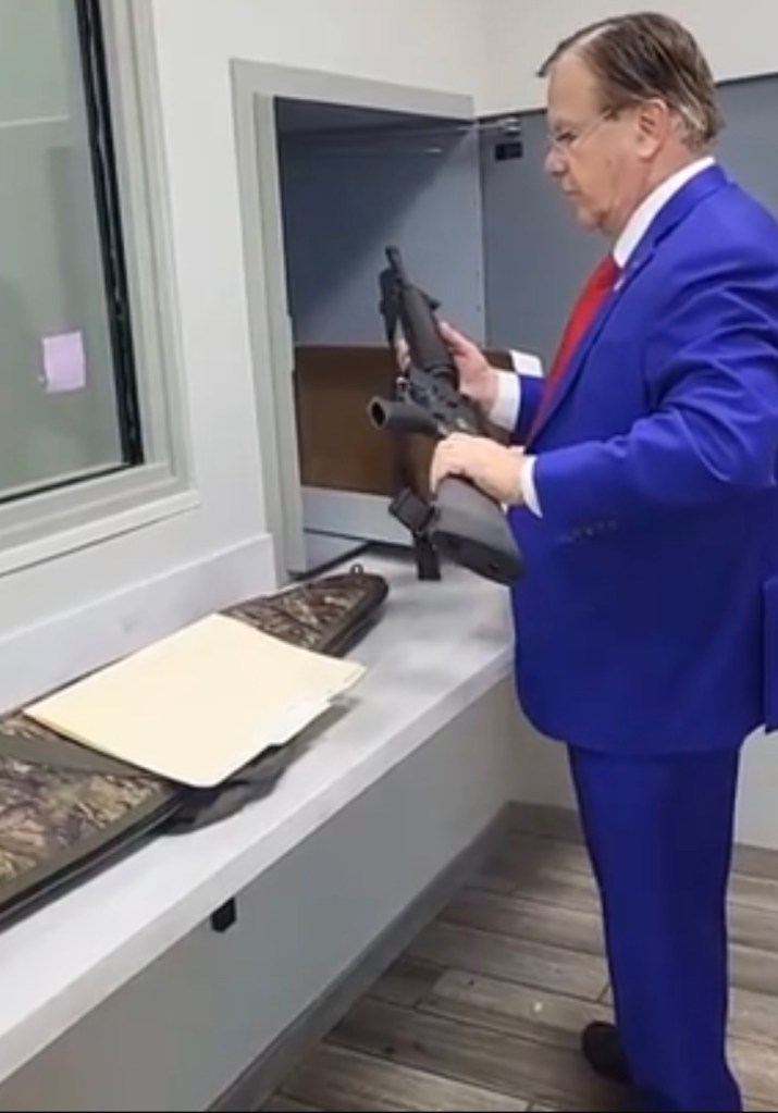 Man in a blue suit retrieving his AR-15 rifle.