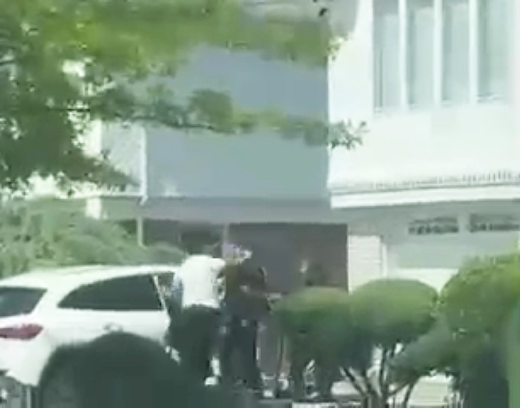 a still from video of the alleged beatdown with a man in a white t-shirt throwing a punch at someone next to a white car