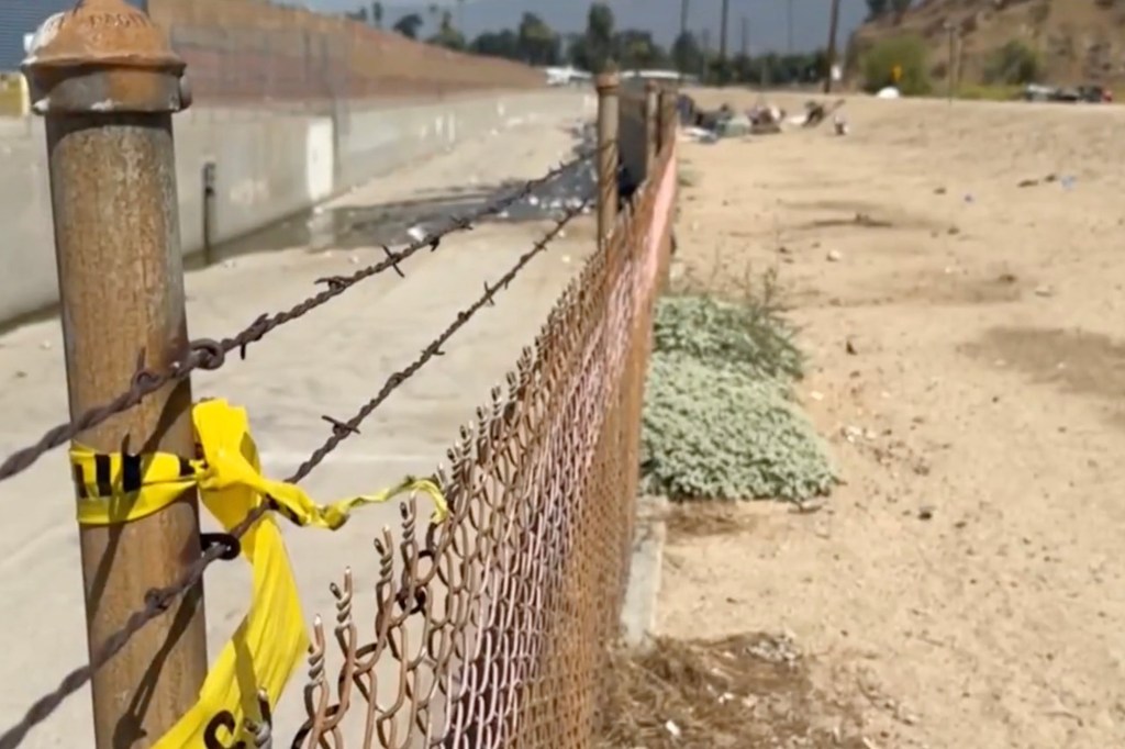 Yellow police tape on a fence near a homeless encampment.