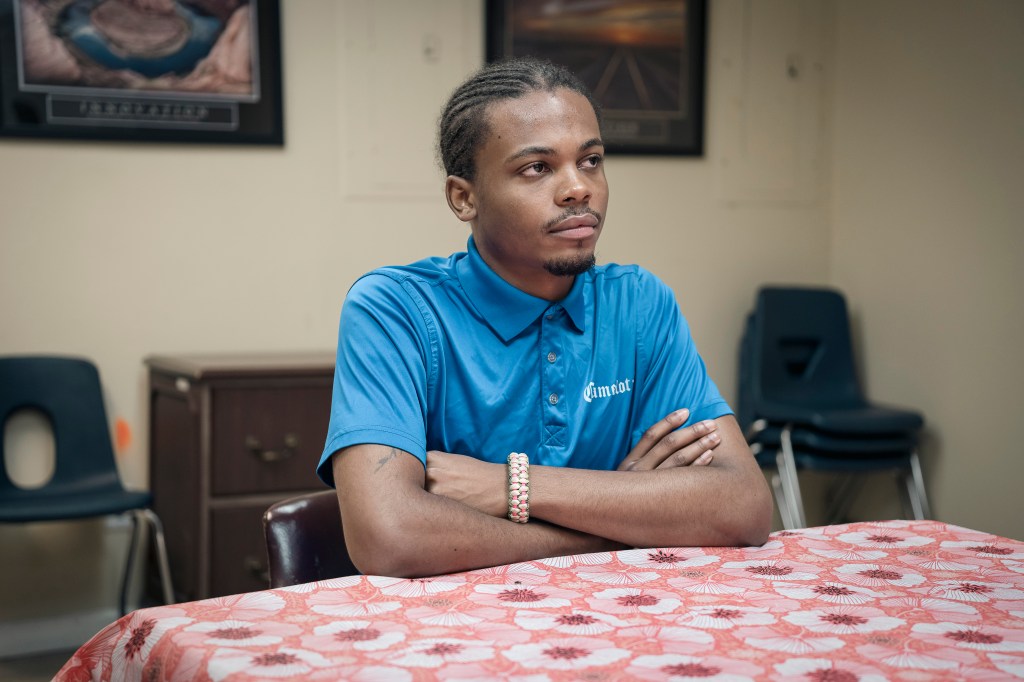 A young man sits at a table with his arms crossed, participating in a marijuana addiction program.