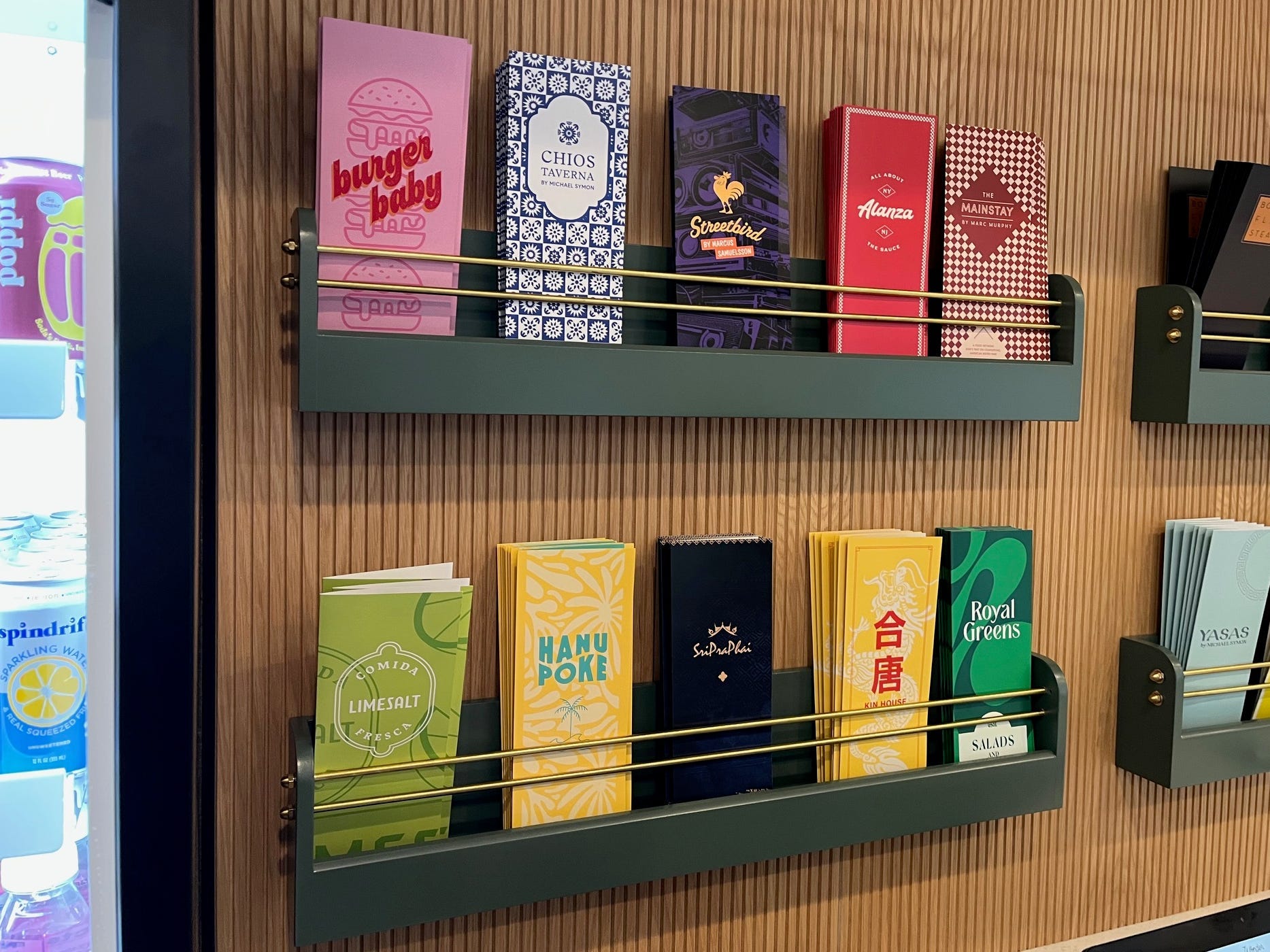 Paper menus from Wonder's various restaurant concepts, including Burger Baby and Streetbird, sit in racks on a wall