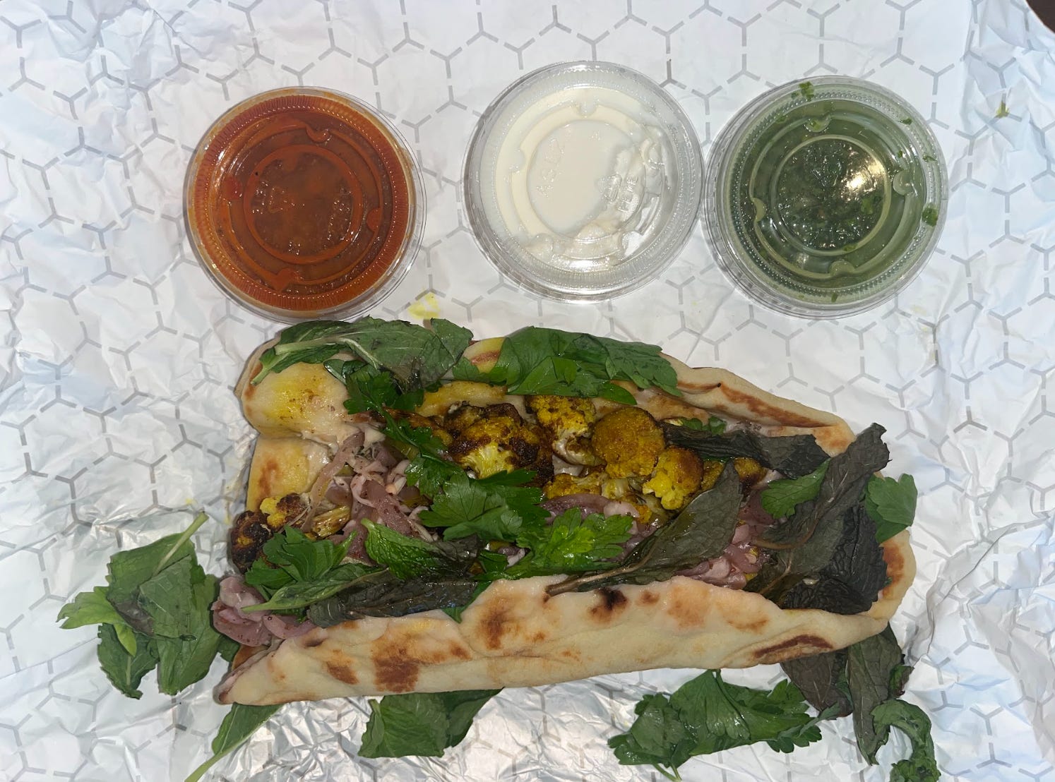 Lamb shawarma from Wonder, served in a pita bread and topped with cilantro. Three dips sit in small cups next to the wrap.
