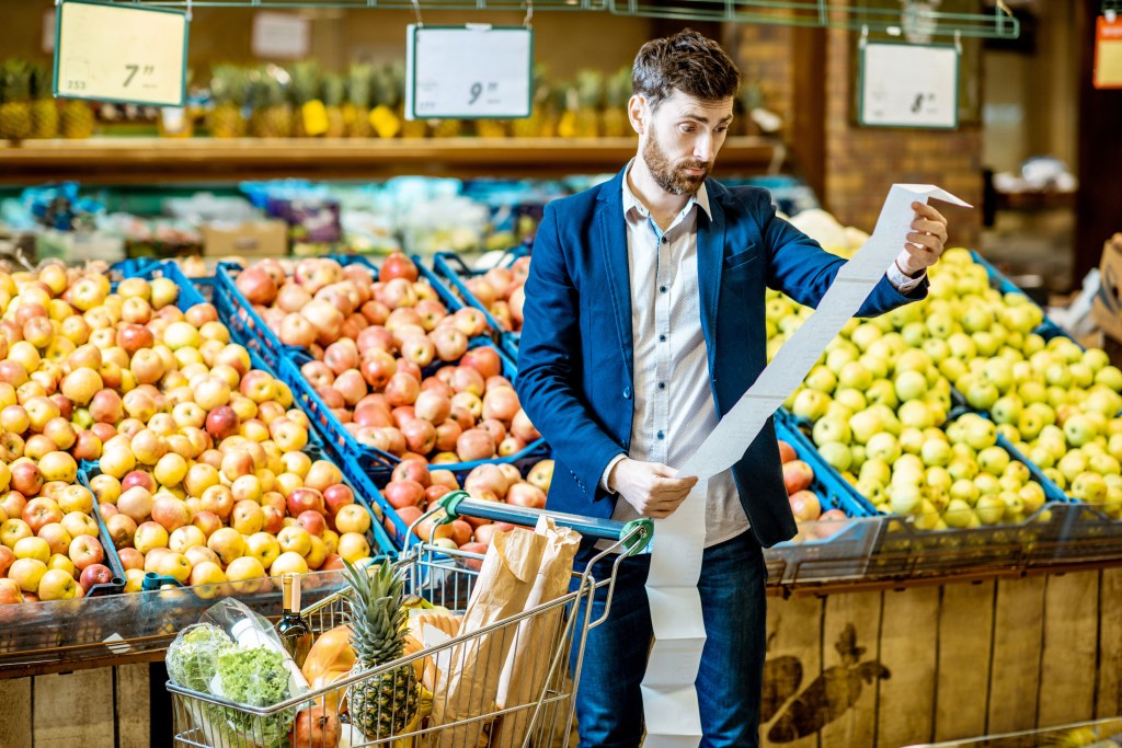 Man comparing shopping list to receipt in supermarket.