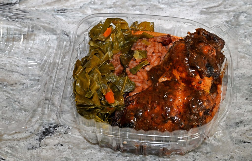Jerk chicken, collard greens, and rice in a plastic container.