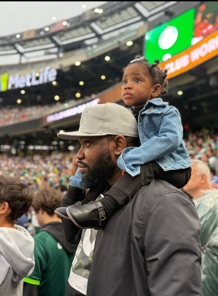 A toddler sits on a man's shoulders at a sporting event.