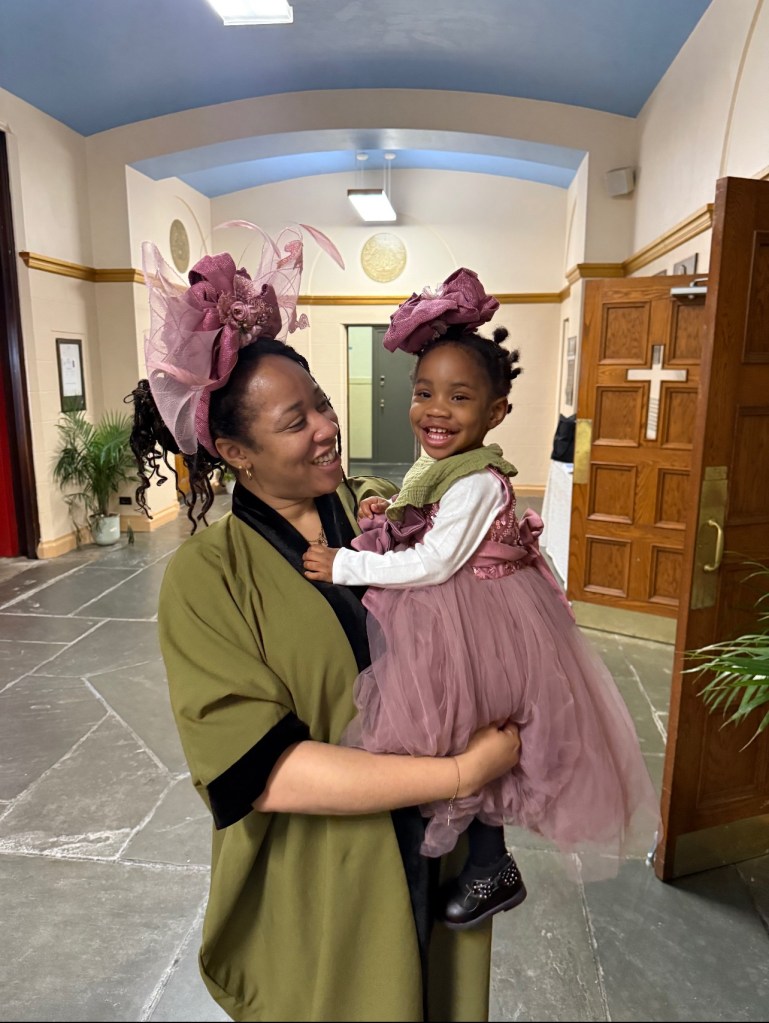 A woman holding a smiling young girl in a pink dress.