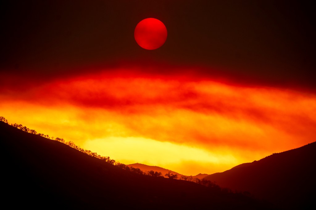 Red sun setting over fire-affected hills.