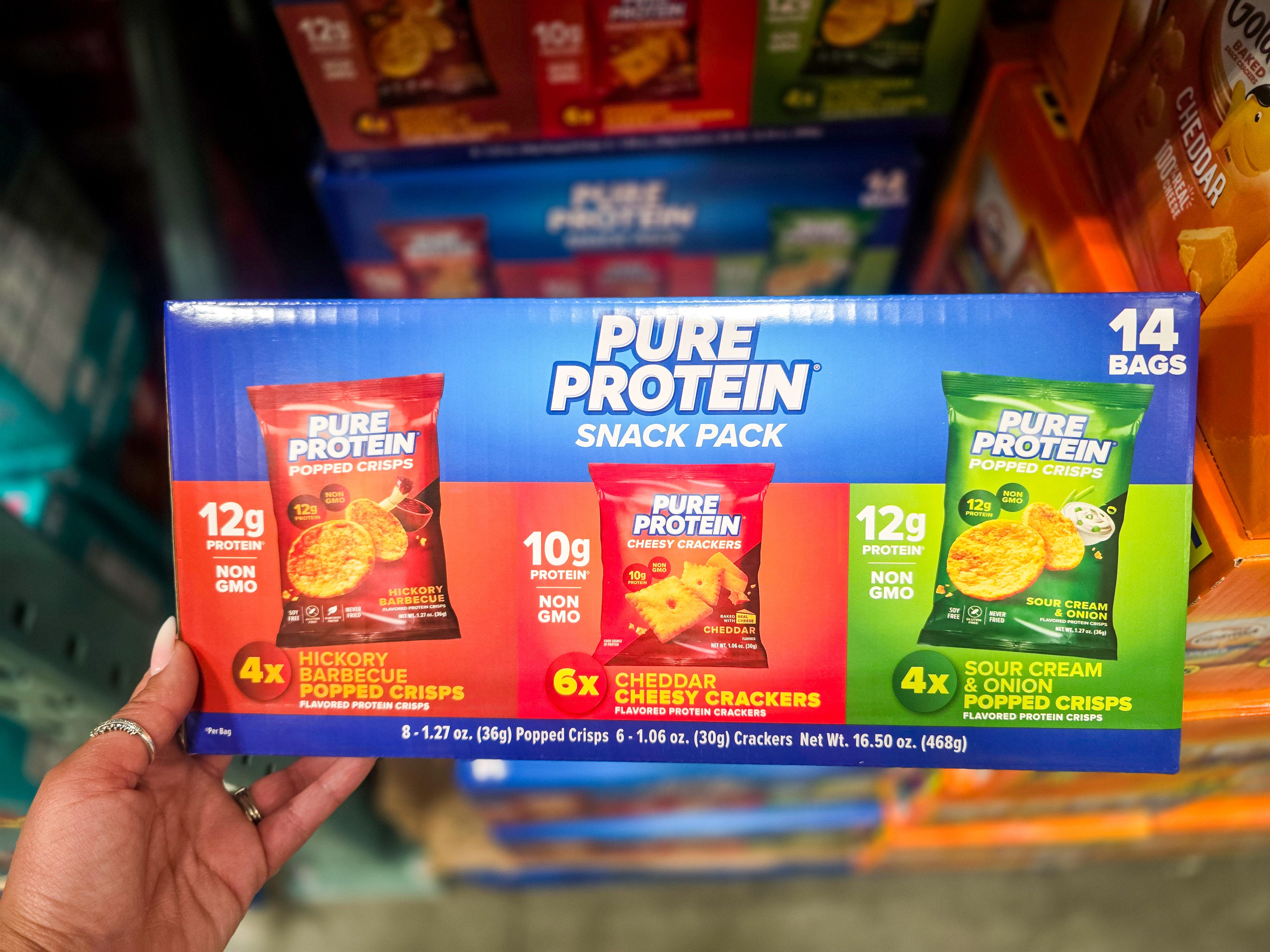 A hand holding a box of Pure Protein snack packs.