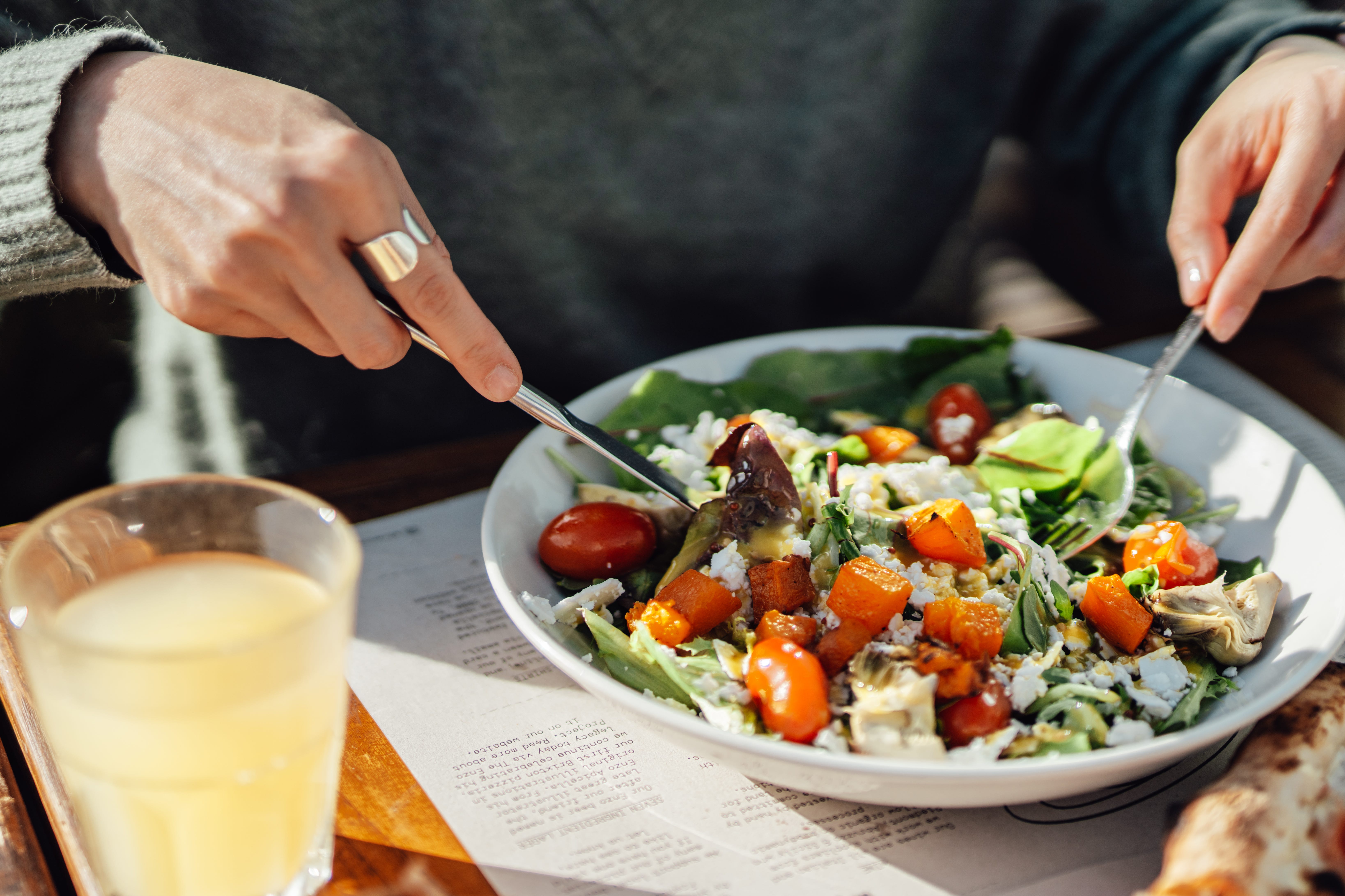 person with fork and knife in a colorful green and orange vegan salad