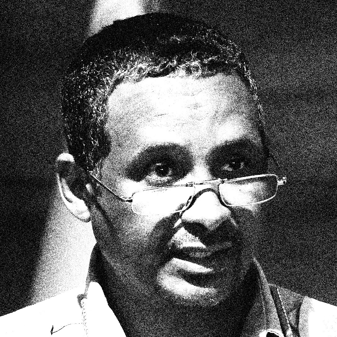 black-and-white photo of man wearing reading glasses and speaking
