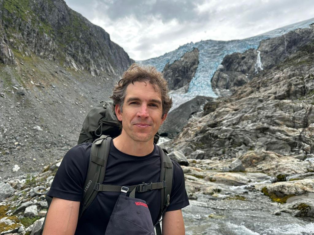 Man with backpack in front of glacier.