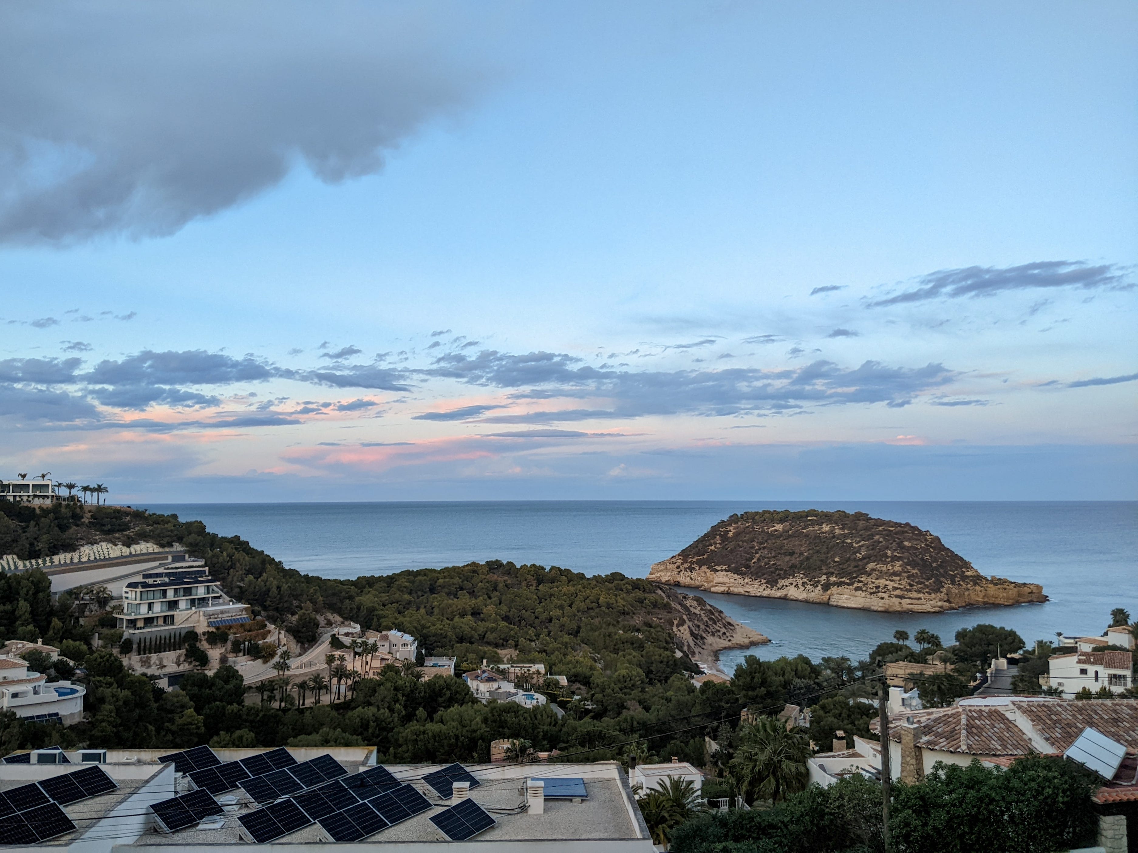 A coastal town with a view of a rocky island at sunset.