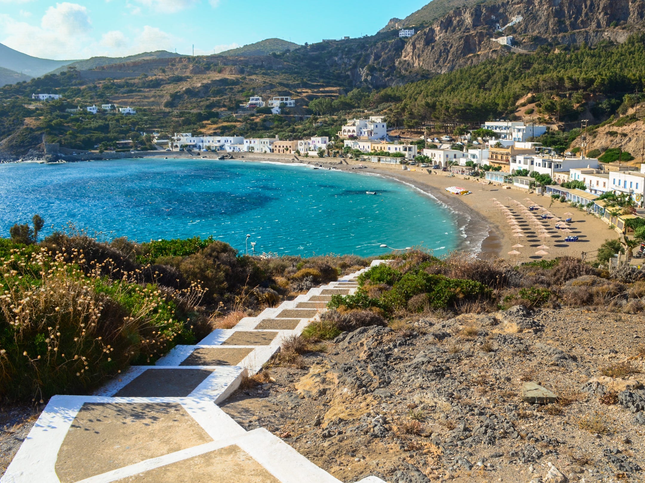 Stairs leading down to a seaside village with mountains in the background.