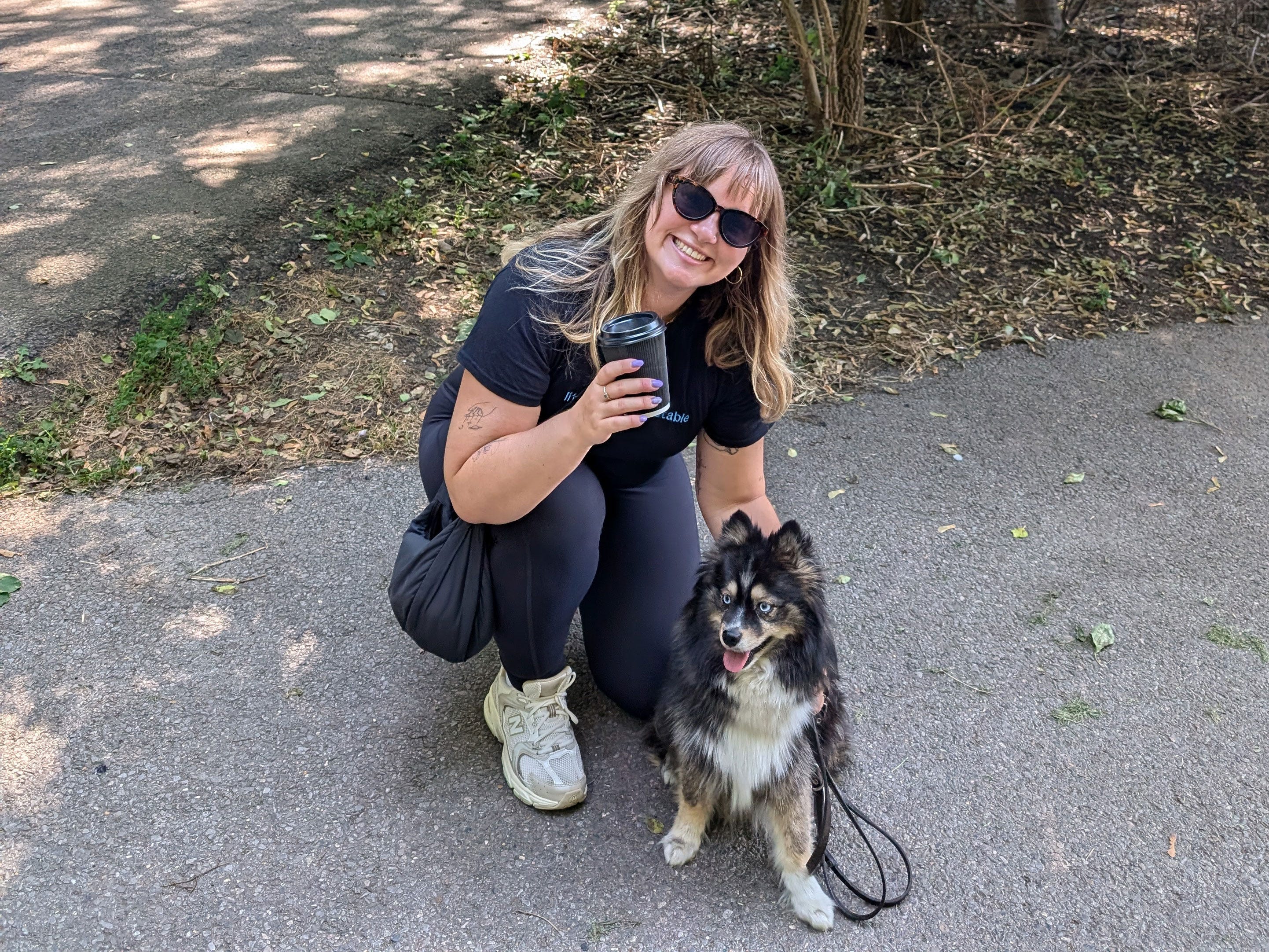 Fleurine squats down next to a small dog, with a coffee cup in her hand.