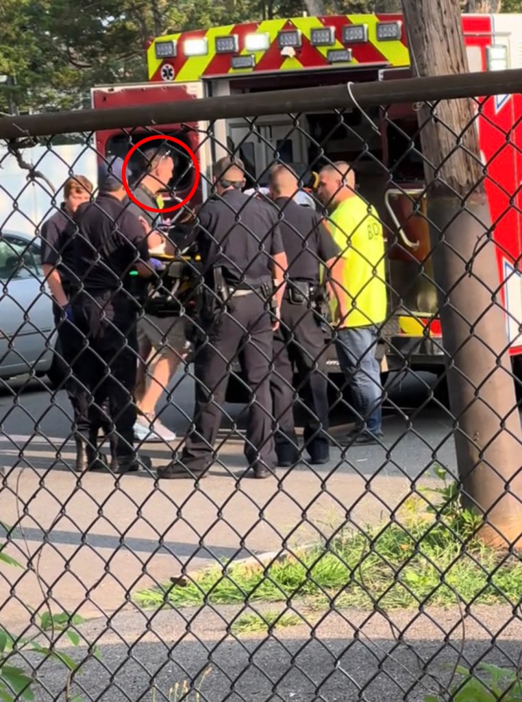 First responders attending to a person on a stretcher behind a chain link fence.