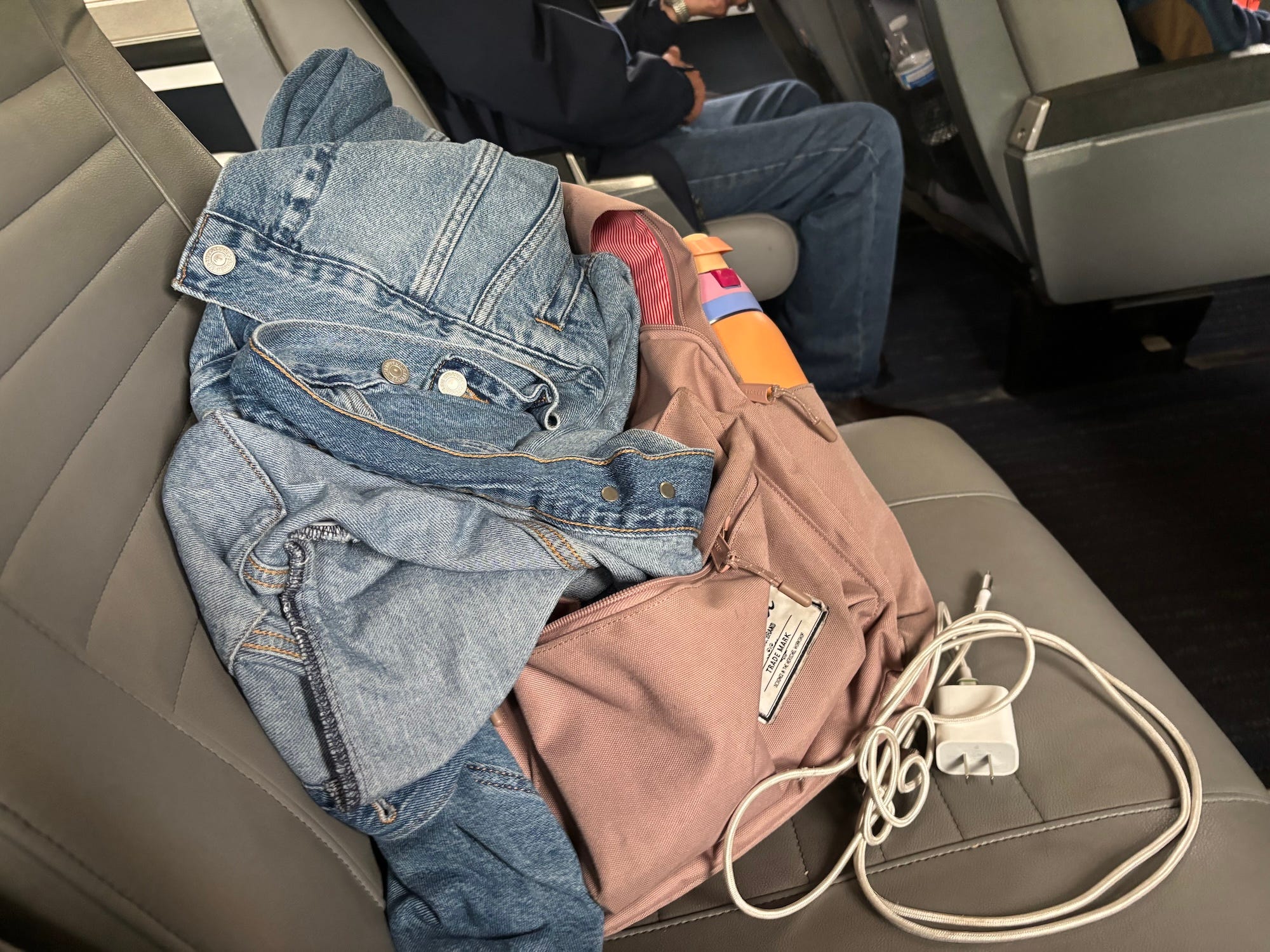 A photo of a backpack, phone charger, and jean jacket piled onto the seat of an Amtrak train.