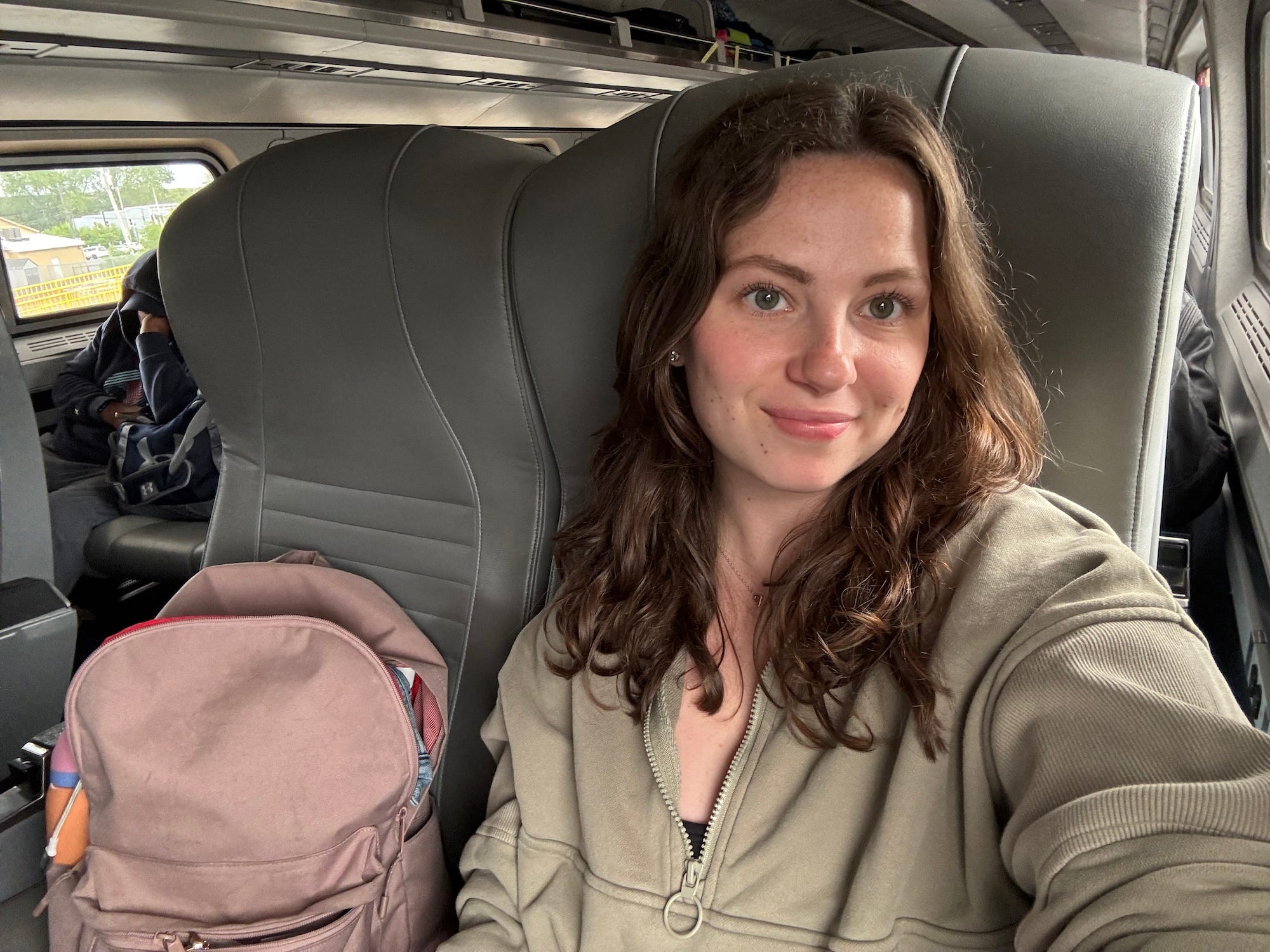 A selfie of a woman sitting on an Amtrak car. A backpack sits in the seat next to her.