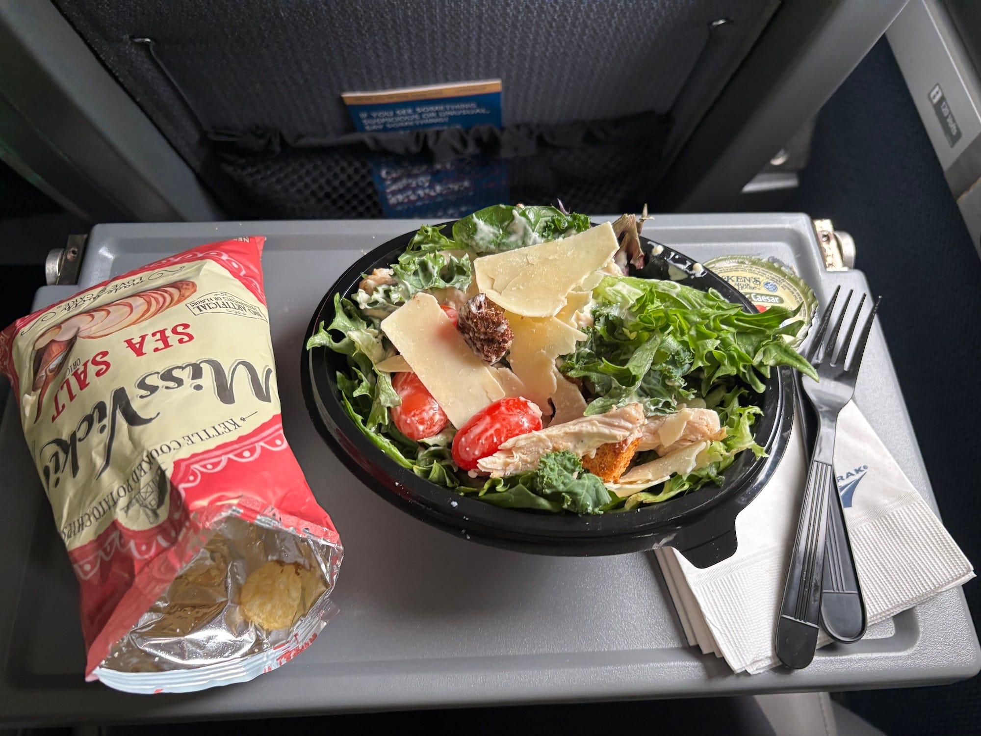 A photo of a bag of chips and a ceaser salad on a tray on an Amtrak train.