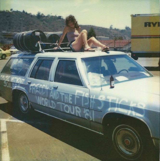 photo of light blue station wagon with woman posing sitting on top next to roof rack with gear strapped to it and 'FREDDY AND THE FISHSTICKS WORLD TOUR '81' hand-painted in white paint along the side